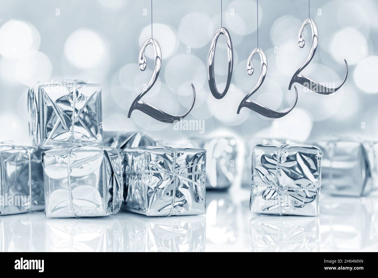 2022, Jahreskarte. Kleine Weihnachtsgeschenke in glänzendem Silberpapier, Bokeh-Lichter Hintergrund Stockfoto