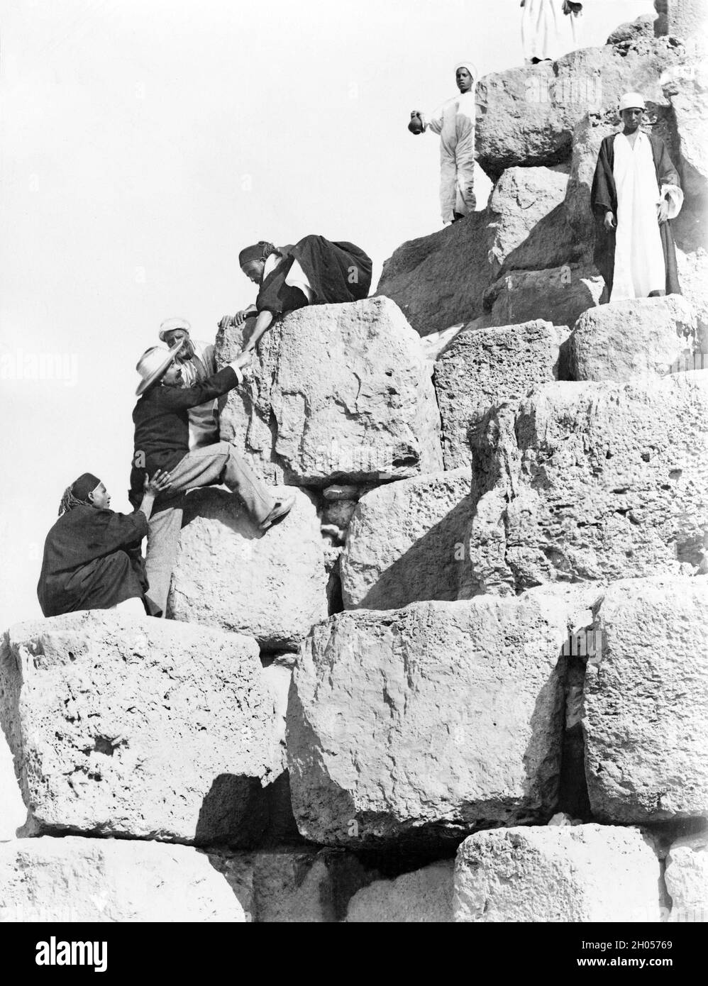 Ein Vintage-Foto aus der Zeit um 1880 von einem Touristen, der von lokalen Ägyptern beim Aufstieg auf die große Pyramide von Gizeh unterstützt wurde. Auch bekannt als die Pyramide von Khufu oder die Pyramide von Cheops. Das Besteigen der Pyramiden ist heute verboten. Stockfoto