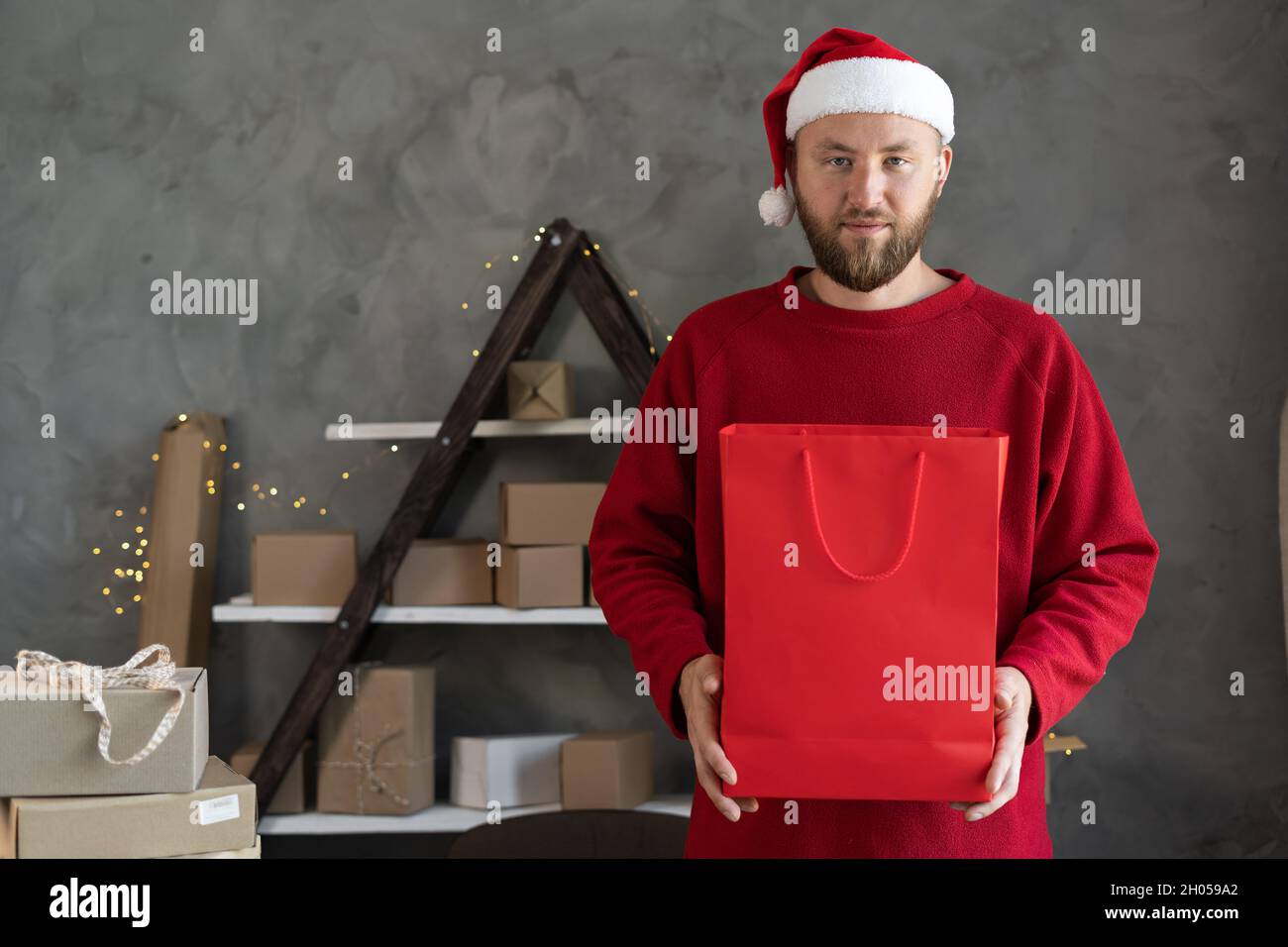 Kaukasischen bärtigen Mann in weihnachtsmann Hut und roten Pullover gibt rote Paket mit Kauf oder Geschenk für Neujahr, Lieferung und Logistik, Online-Verkäufer Stockfoto