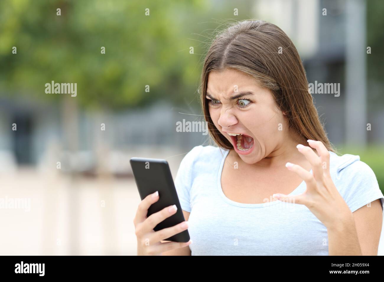 Wütender Teenager, der in einem Park Medien auf dem Smartphone ansieht Stockfoto