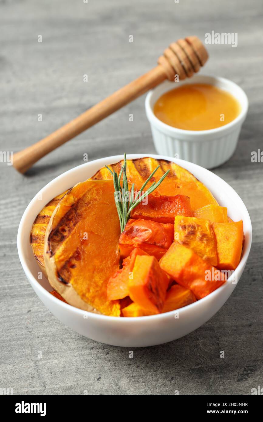 Gebackener Kürbis, Honig und ein Löffel auf einem grauen strukturierten Hintergrund, eine süße Herbstdessert-Idee Stockfoto