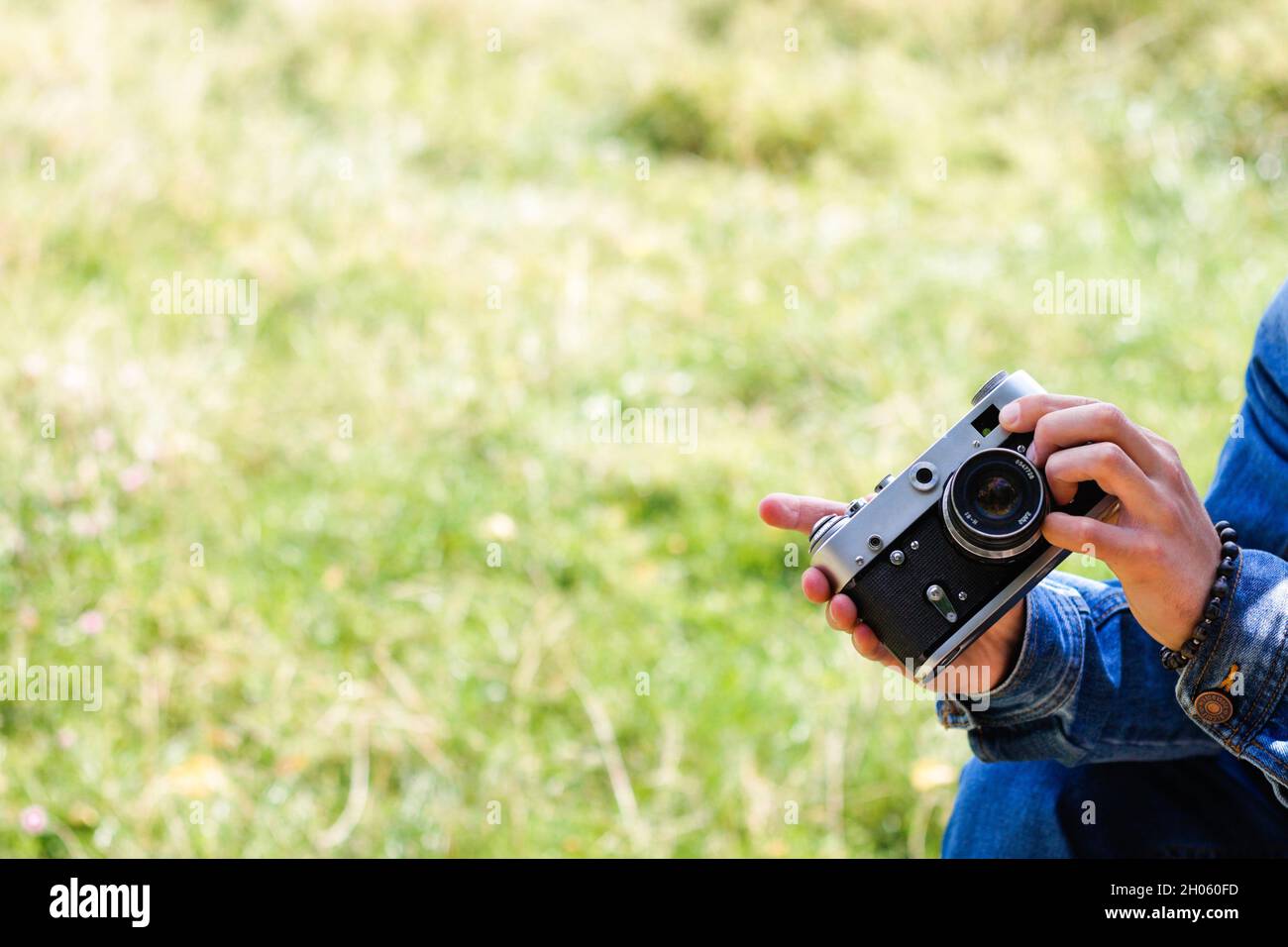 Unschärfe-männliche Hände halten Retro-Fotokamera auf hellgrünen Natur Hintergrund. Speicherplatz kopieren. Filmkorneffekt. Mann in Jeans fotografiert auf Vintage Ca Stockfoto
