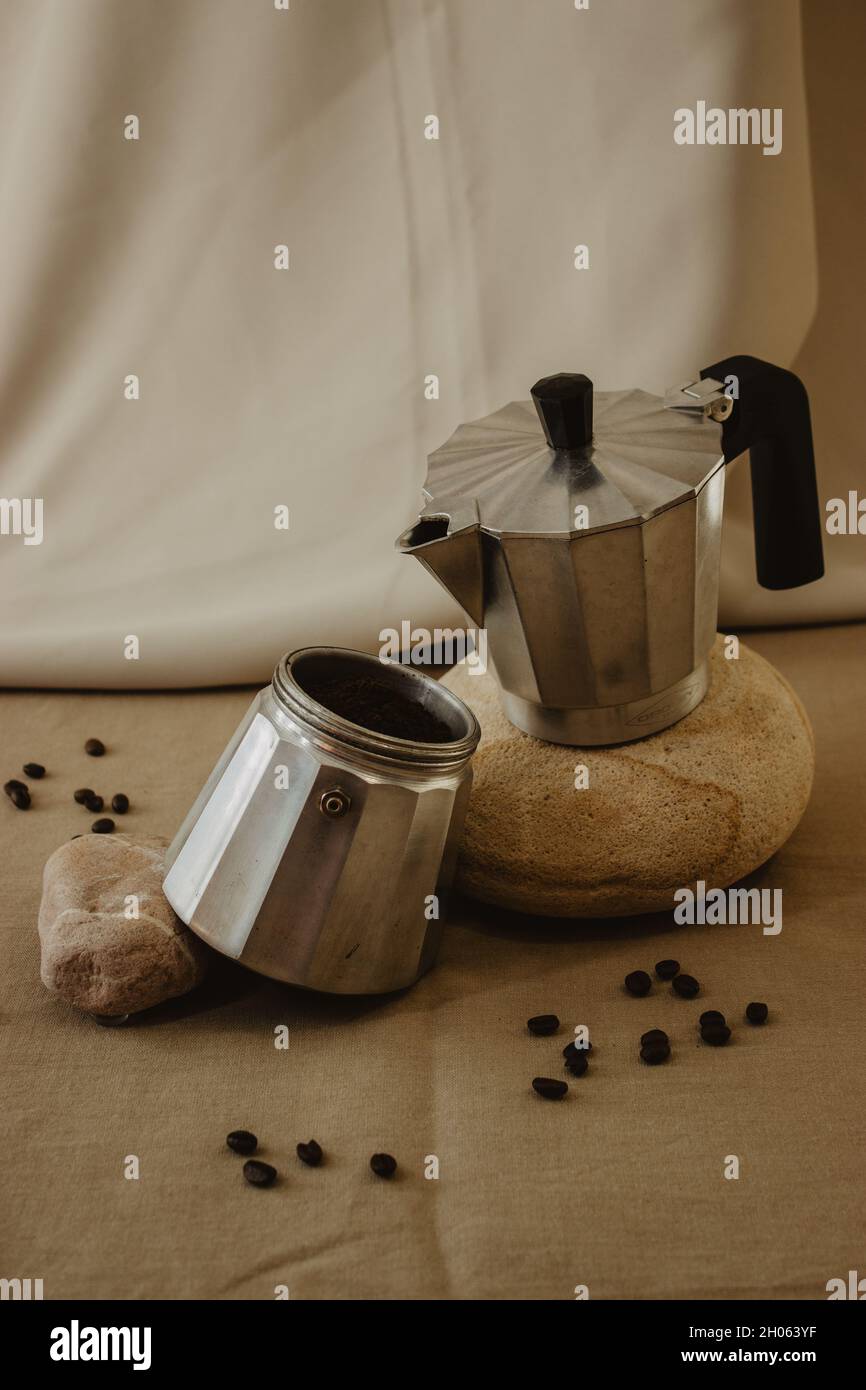 Kaffeekocher aus Metall auf einem Stein mit Kaffeebohnen und Kaffeepulver auf einem isolierten beigen Hintergrund. Stockfoto