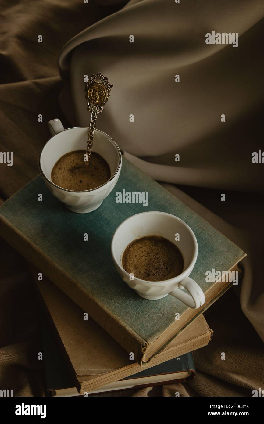 Zwei Kaffeetassen mit einem Original-Löffel auf Büchern auf einem isolierten beigen Hintergrund. Stockfoto