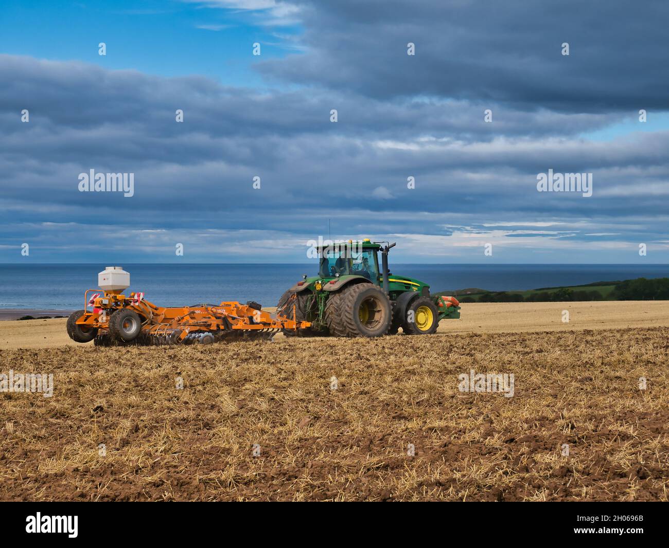 Ein grüner John Deere Traktor, der an einem teilweise sonnigen Herbsttag ein Feld mit Stoppeln pflügt. Aufgenommen in Northumberland, England, Großbritannien Stockfoto