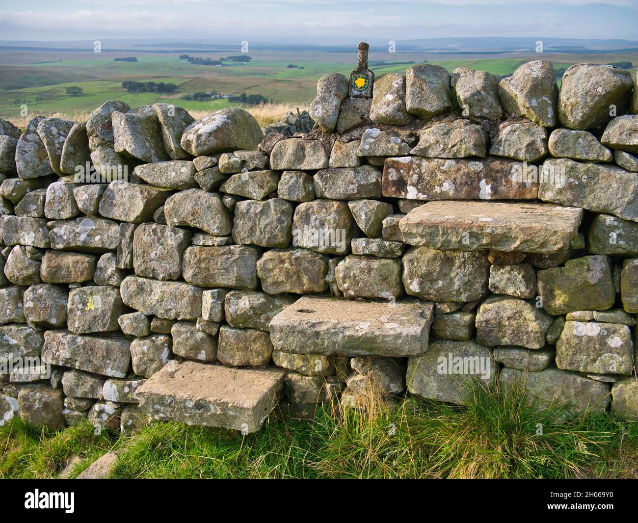 Drei verwitterte, freitragende Stufen in einer trockenen Steinmauer bilden einen Stelzenbau an einer Feldgrenze auf dem Hadrian's Wall Path in Northumberland, England, Großbritannien. Stockfoto