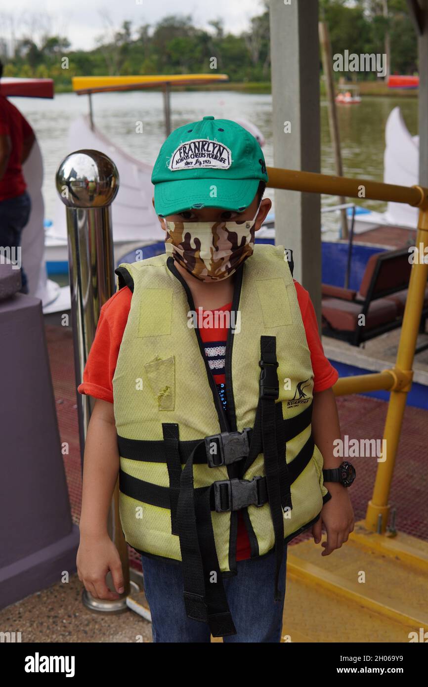 Ein Kind, das eine Sicherheitsweste trägt, bevor es entlassen wurde, um ein Familienpaddelboot im City Lake Park Kuantan Malaysia zu spielen. Stockfoto