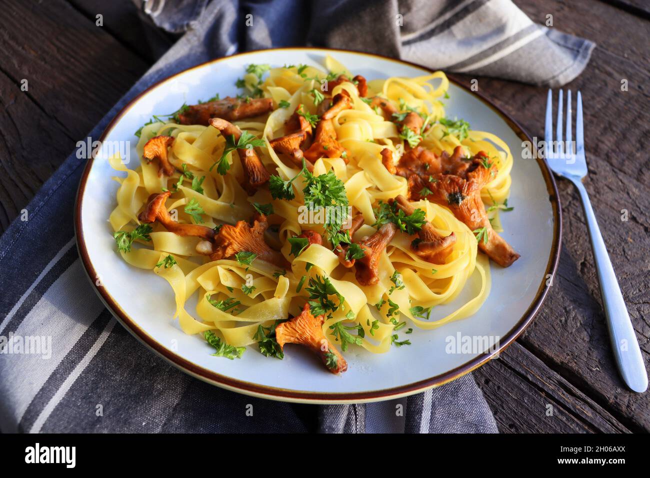 Tagliatelle-Pasta mit gebratenen in Butter gebackenen Pfifferlingen mit Knoblauch und fein gehackter Petersilie auf karierter Serviette auf rustikalem Hintergrund Stockfoto