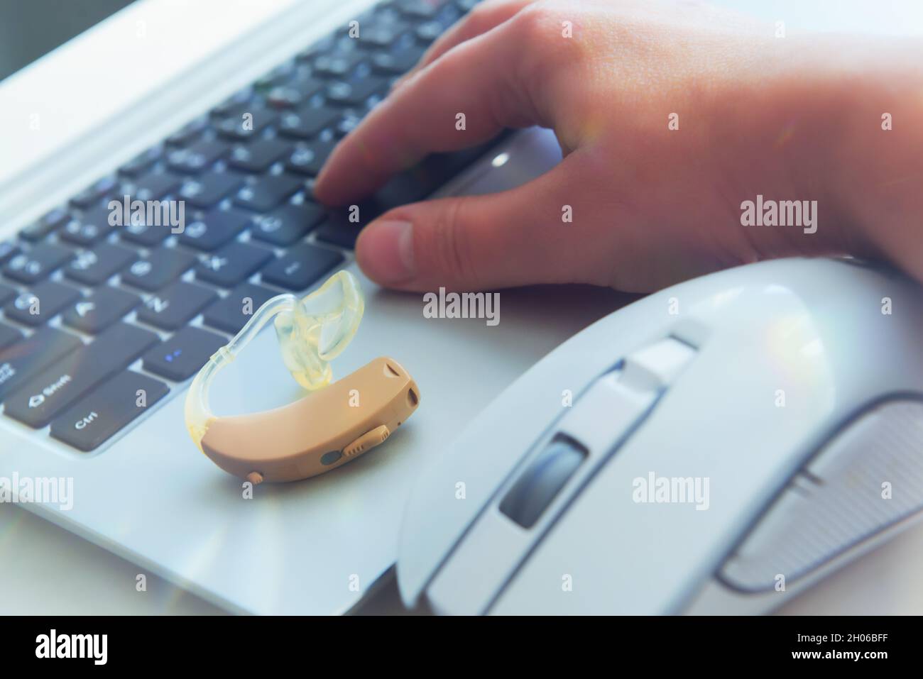 Hörgerät, Frauenhand auf Laptop-Tastatur und Computermaus. Arbeit für gehörlose Menschen Stockfoto