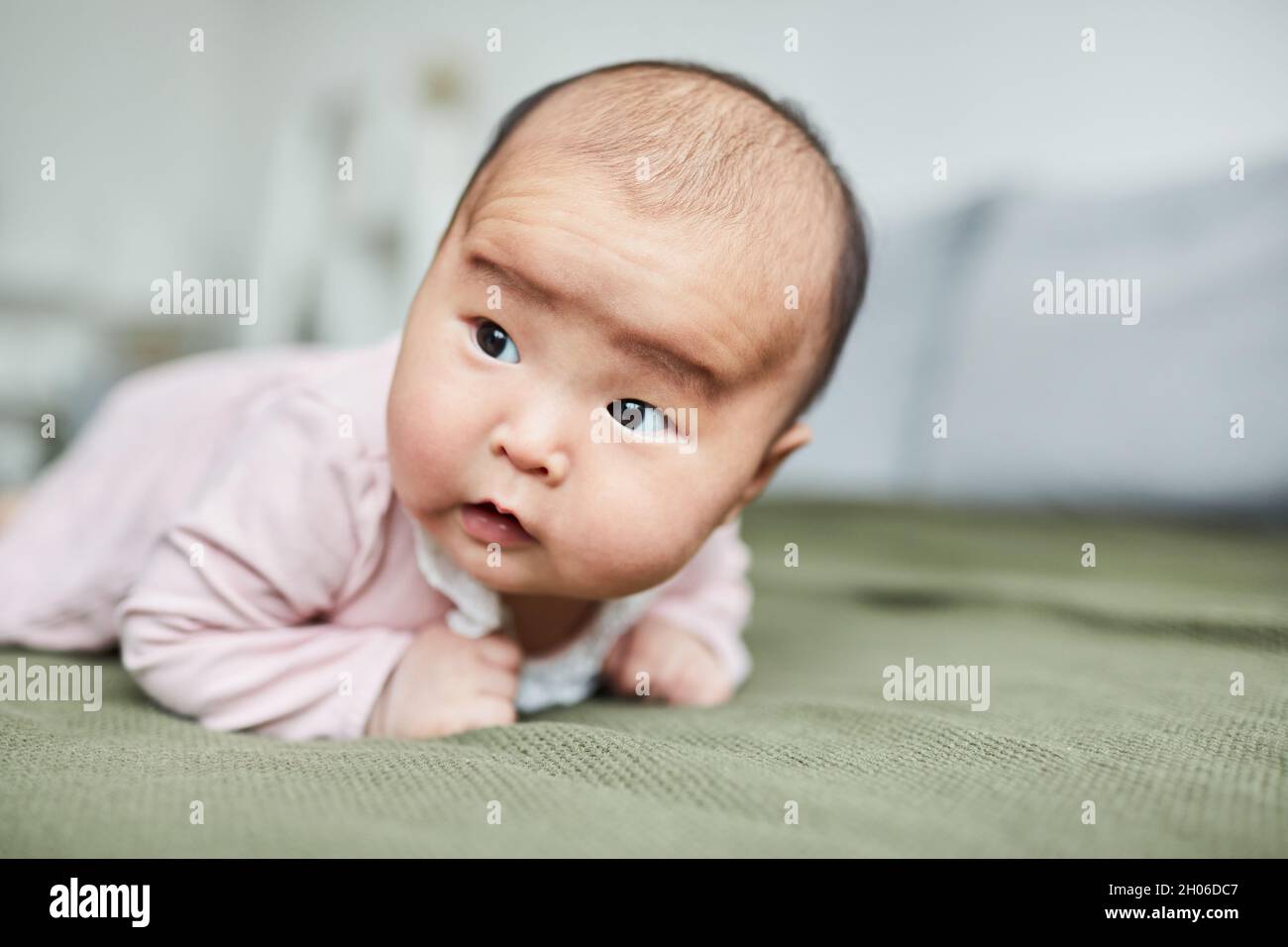 Nahaufnahme eines niedlichen Babys, das lernt, auf dem Bett im Zimmer auf dem Bauch zu liegen Stockfoto