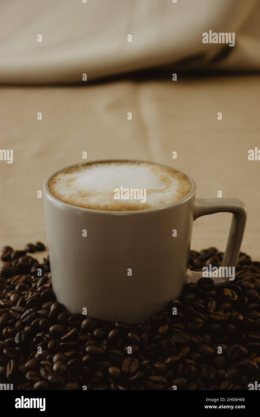 Tasse Latte-Kaffee am Boden der Kaffeebohnen auf braunem Hintergrund. Stillleben Kaffeefotografie. Stockfoto