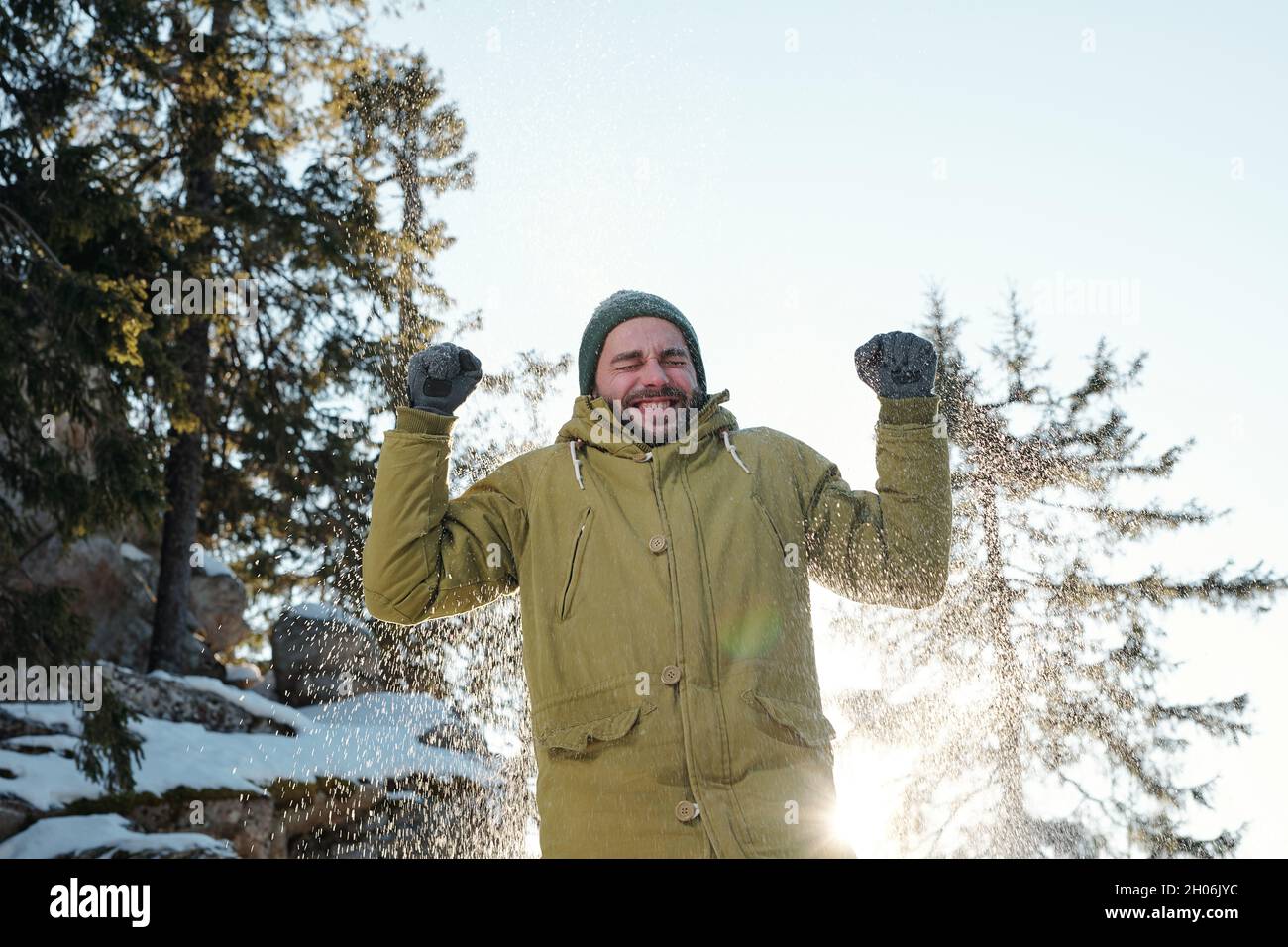 Lächelnder junger Mann, der Schneefall genießt, während er das Wochenende im Winterwald verbringt Stockfoto