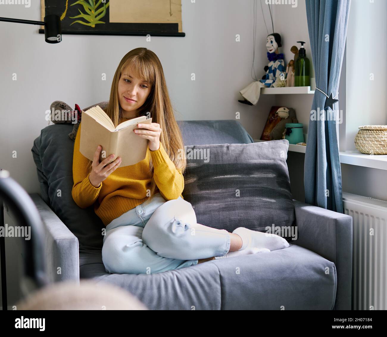 Junge Frau, die auf dem Sofa sitzt und begeistert Buch liest. Konzept der digitalen Entgiftung Stockfoto