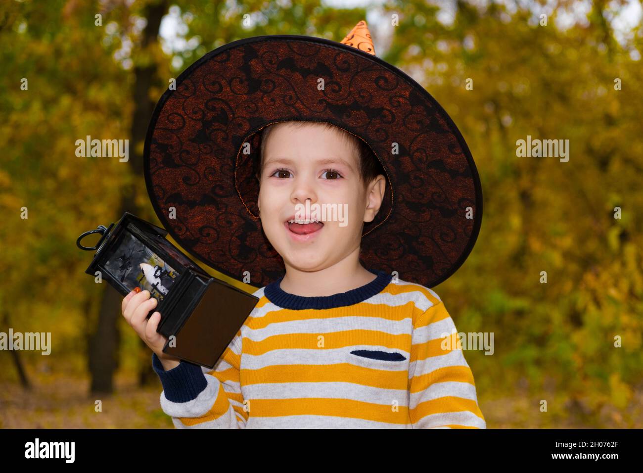 Halloween-Kind in einem Hut hält eine Laterne und lächelt Stockfoto
