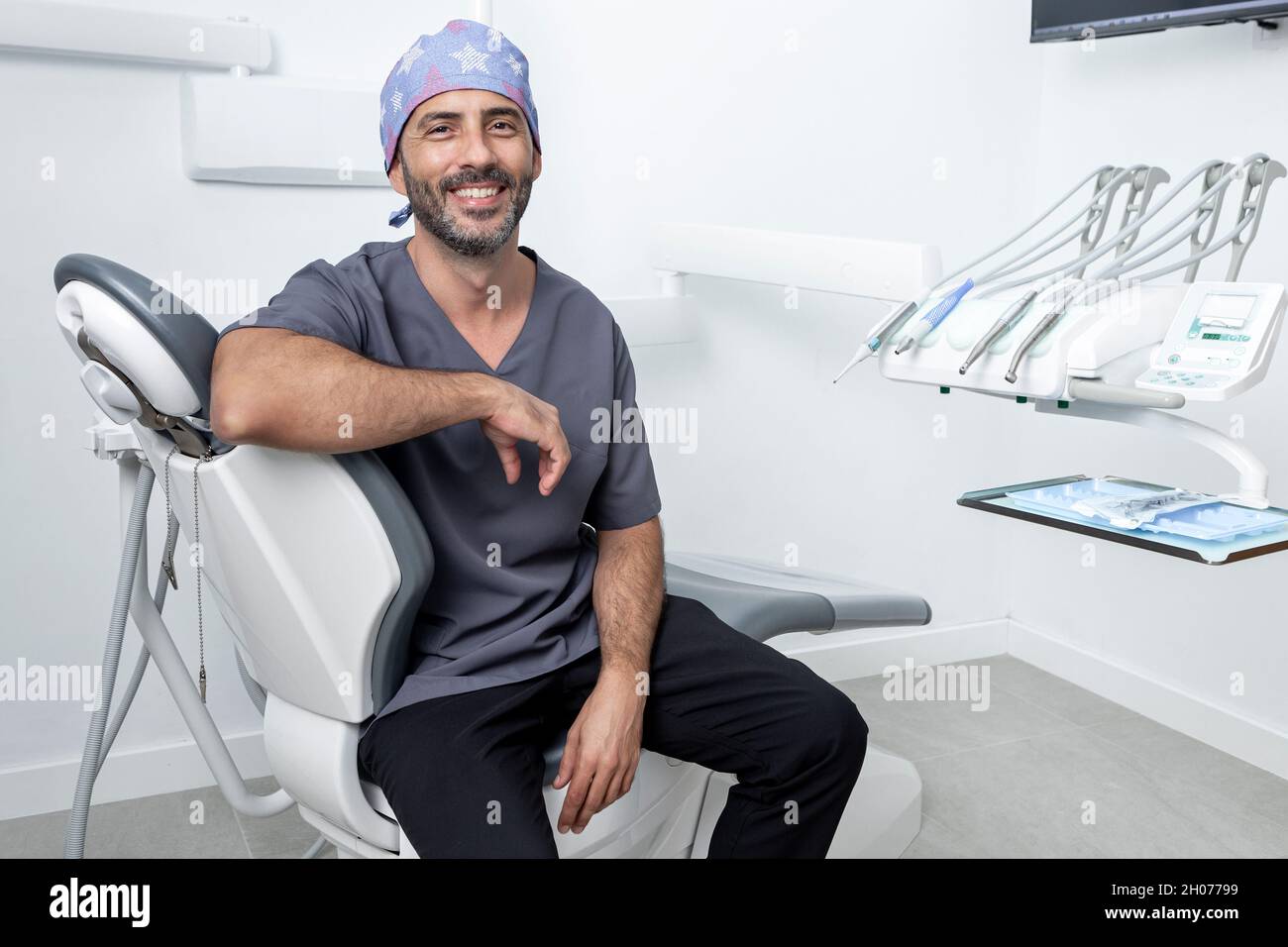 Porträt eines männlichen Zahnarztes mit Uniform, der sich auf einer Bahre in einer Zahnklinik stützt Stockfoto