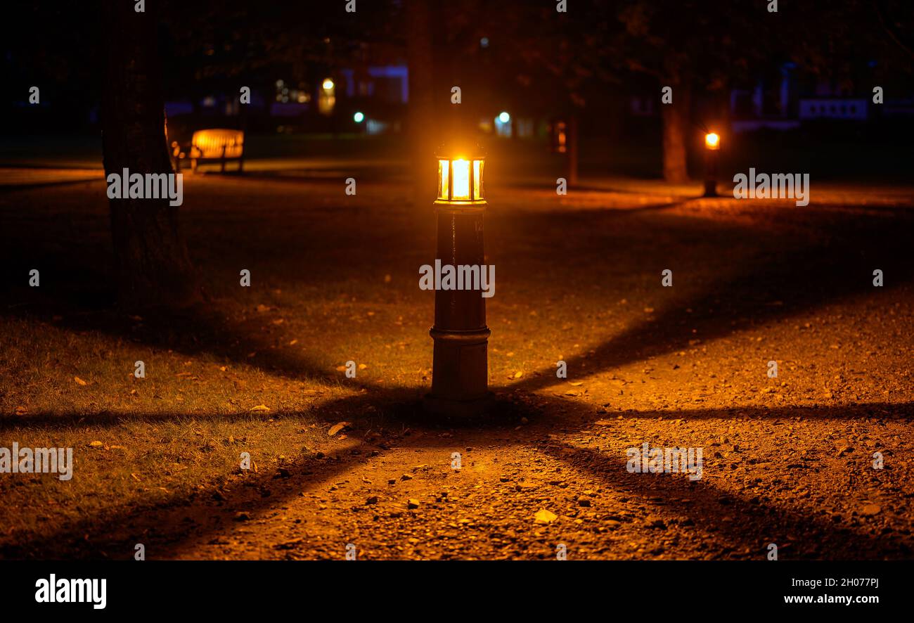 Lampe oder Licht in der Nacht in einem Park mit Schatten in einem kreisförmigen Muster. Das Licht beleuchtet einen steinigen Weg. Symmetrische Ansicht der Lampe und der Schatten. Stockfoto