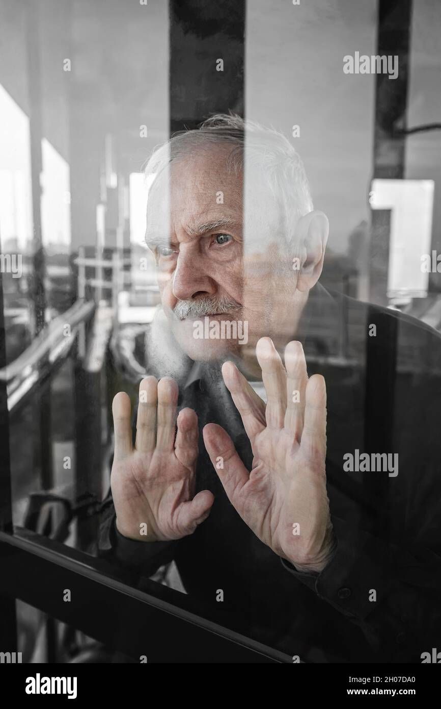 Einsamer alter Mann schaut aus dem Fenster und wartet. Das Konzept der Einsamkeit, des Alters, der Pandemieprobleme, der fehlenden Kommunikation. Quarantäneisolierung. Stockfoto