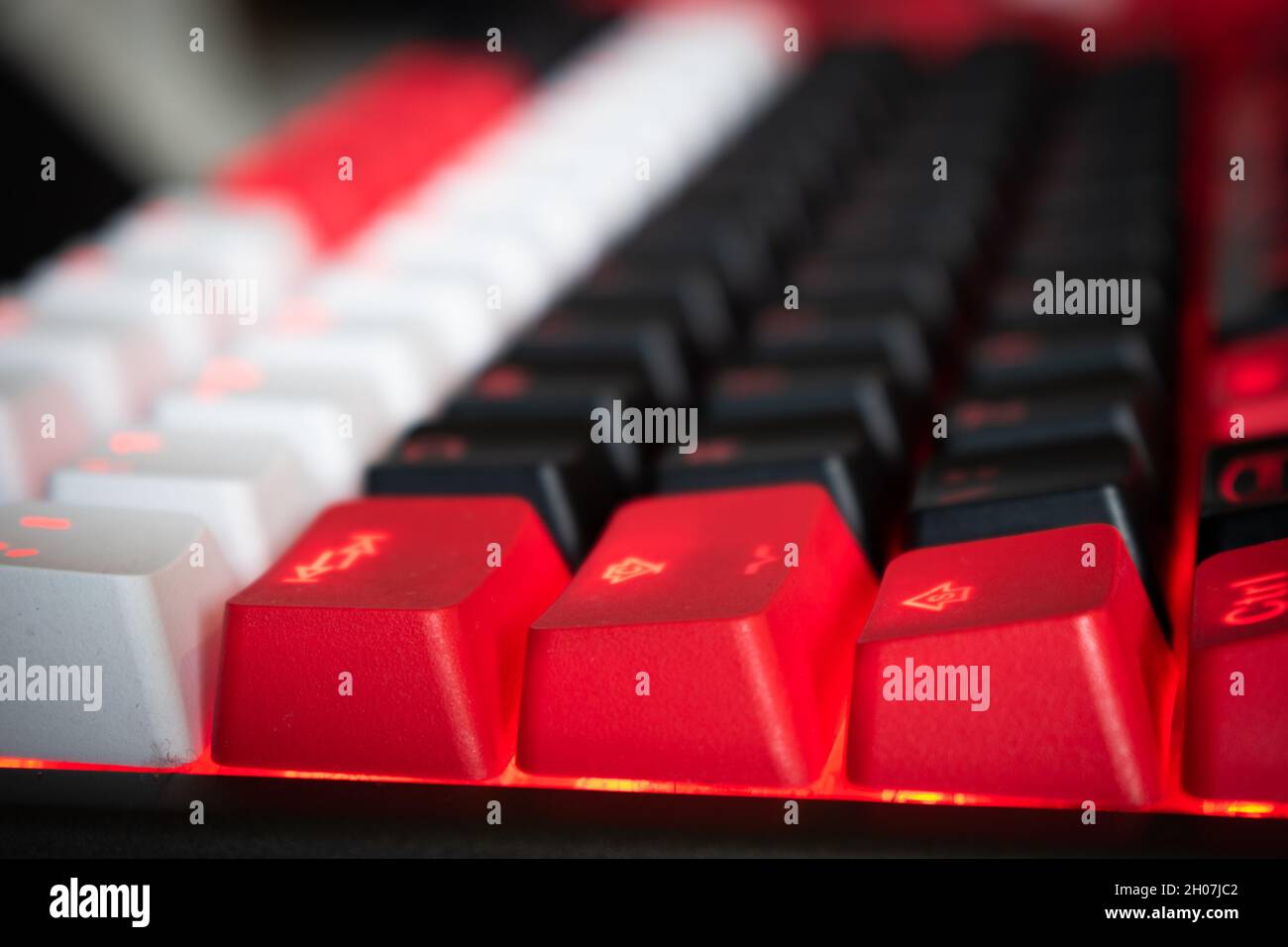 Mechanische Tastatur mit roter Hintergrundbeleuchtung und schwarzen, weißen und roten Tastenkappen in einem Winkel Stockfoto
