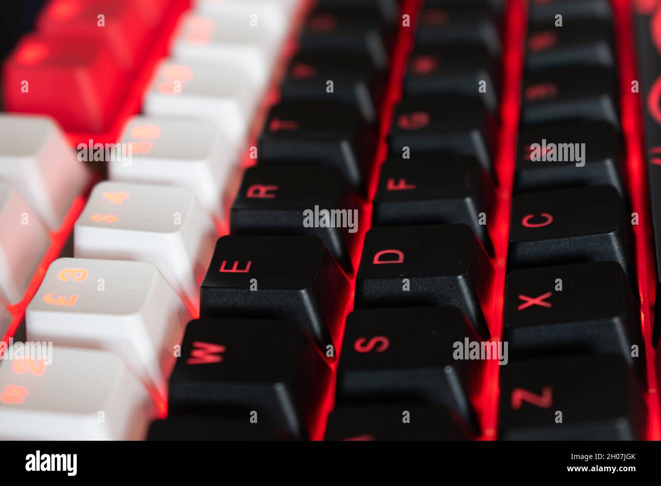 Mechanische Tastatur mit roter Hintergrundbeleuchtung und schwarzen, weißen und roten Tastenkappen in einem Winkel Stockfoto