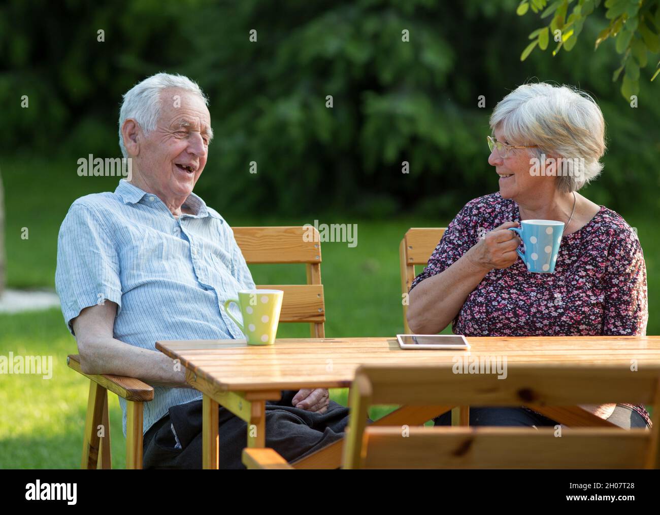 Seniorenpaar sitzt am Holztisch im Garten und trinkt Tee Stockfoto