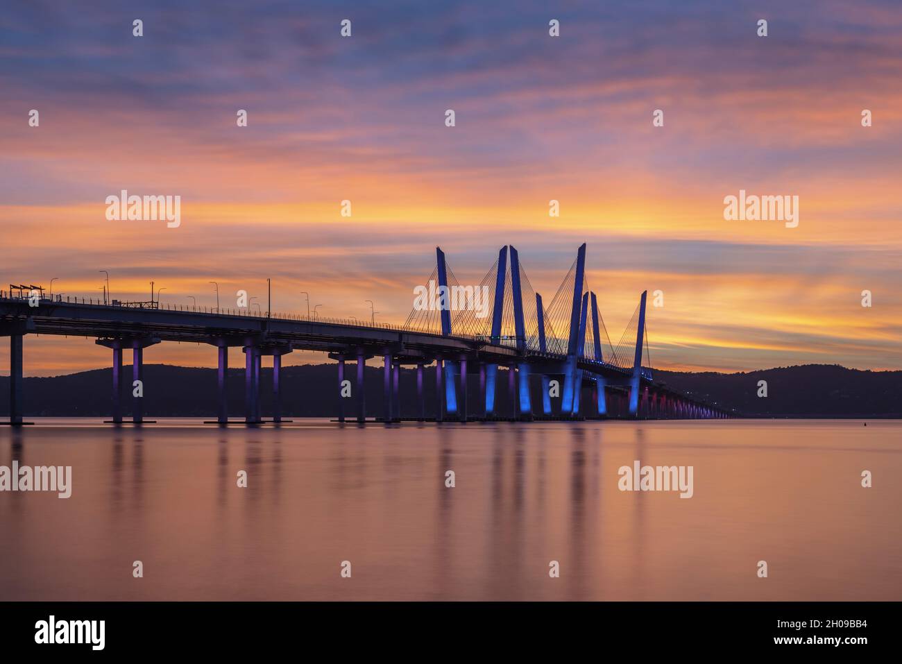 Die Governor Mario M. Cuomo Bridge, in Rot, Weiß und Blau zur Anerkennung des Columbus Day beleuchtet, überspannt den Hudson River kurz vor Sonnenuntergang. Stockfoto