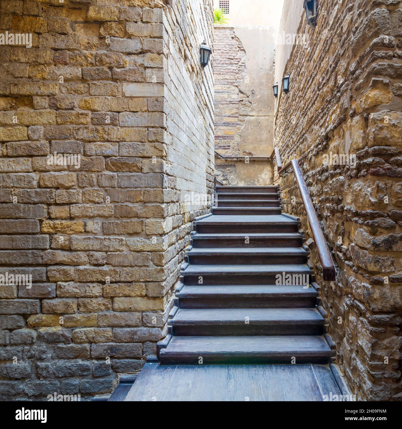Außenaufnahme einer Steinmauer mit einer schmalen, verwitterten Holztreppe, die mit einem hölzernen Handlauf in einem verlassenen Gebäude nach oben führt Stockfoto