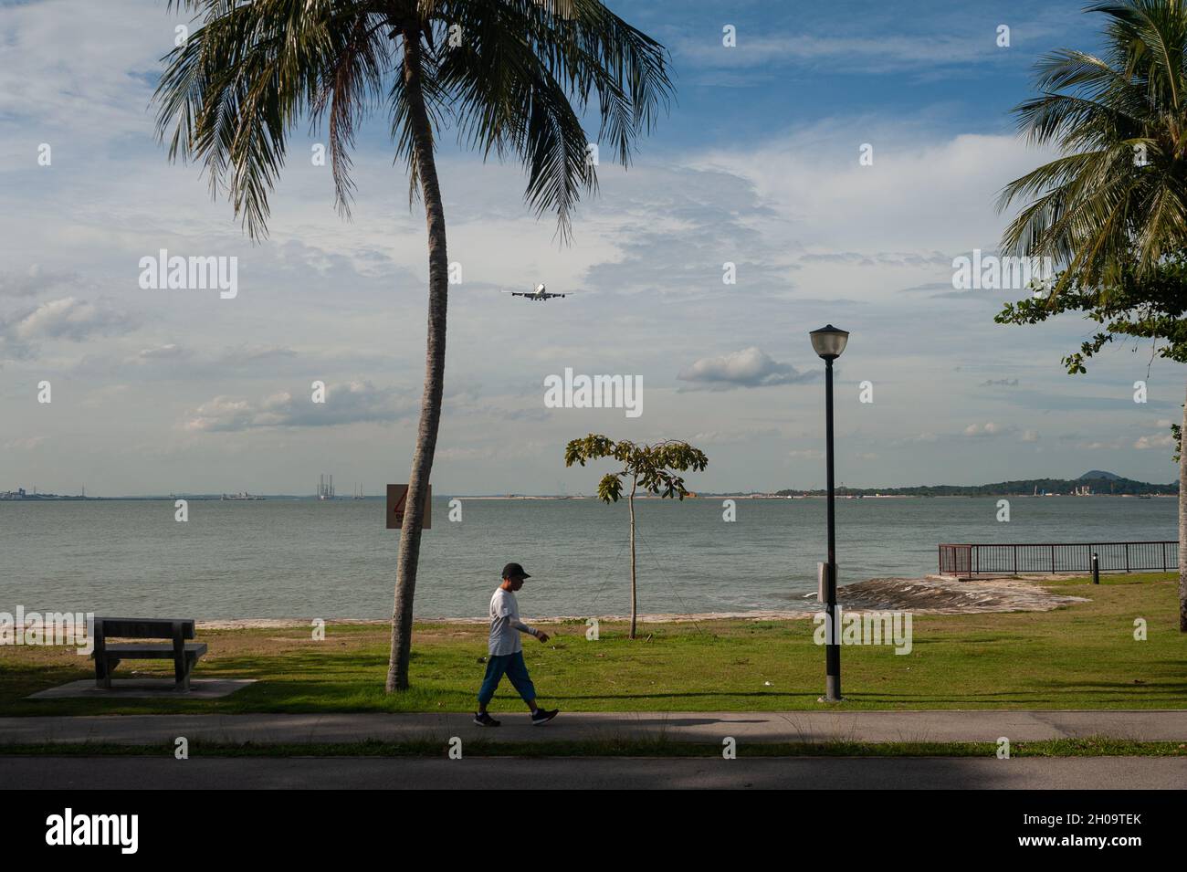 '30.06.2021, Singapur, , Singapur - Ein Mann läuft während der anhaltenden Corona-Krise am Ufer des Changi Beach Parks entlang, während im Hintergrund ein ai Stockfoto