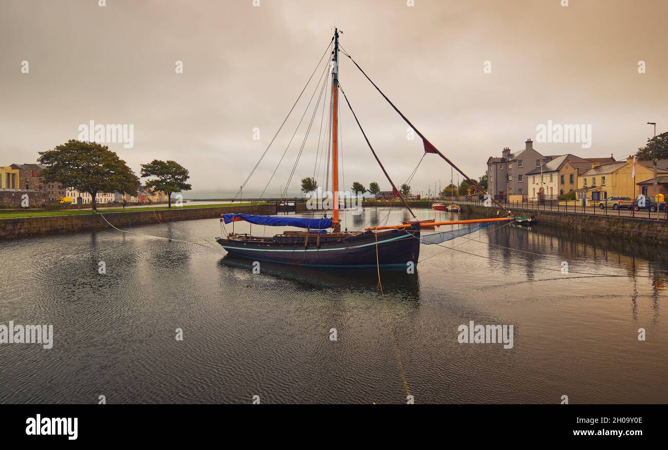 Wunderschöne Stadtlandschaft mit einem alten hölzernen Fischerboot namens Galway Hooker im Corrib River mit bunten Häusern im Hintergrund bei Claddagh in Galway City, Irland Stockfoto