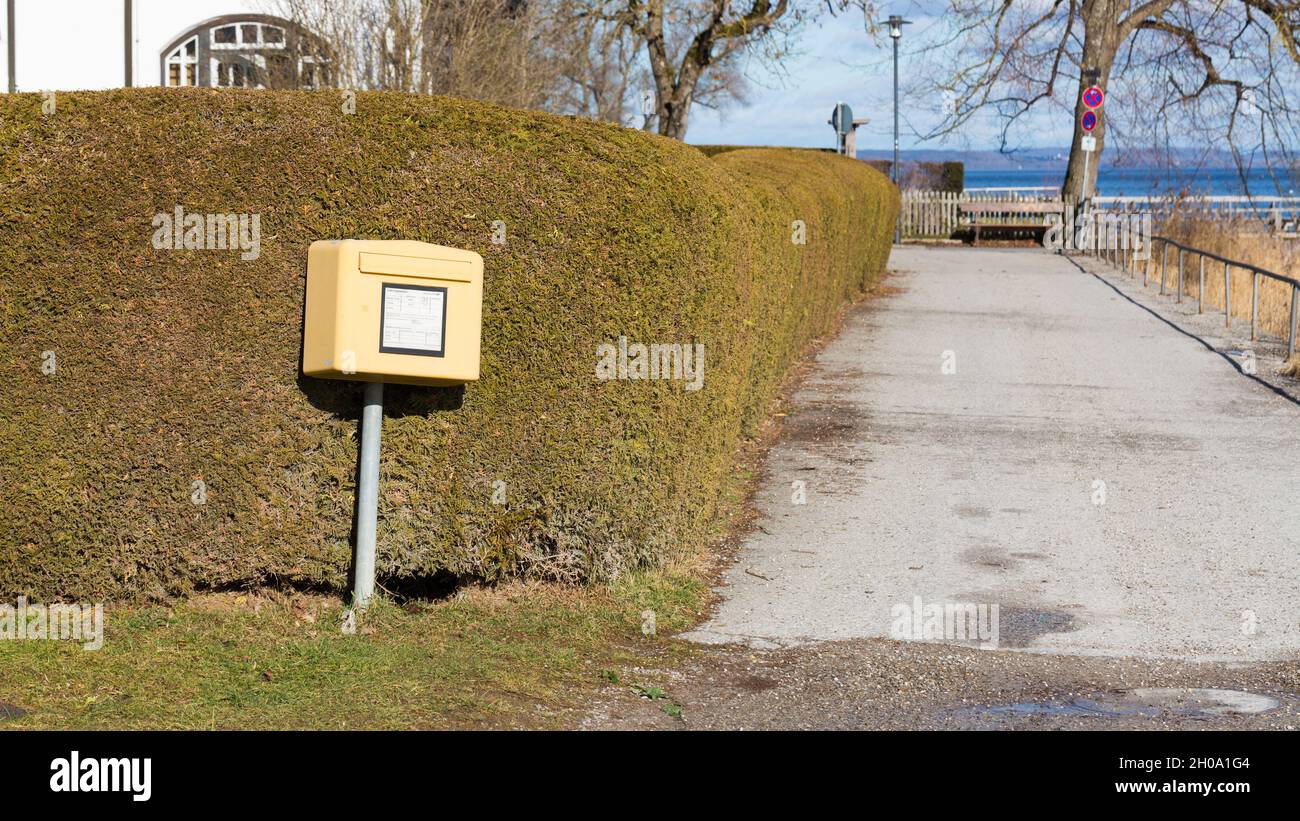 St. Alban, Deutschland - 2. Feb 2021: Gelbe Briefkasten der Deutschen Post vor einem grünen Busch, neben einer kleinen Straße. Stockfoto