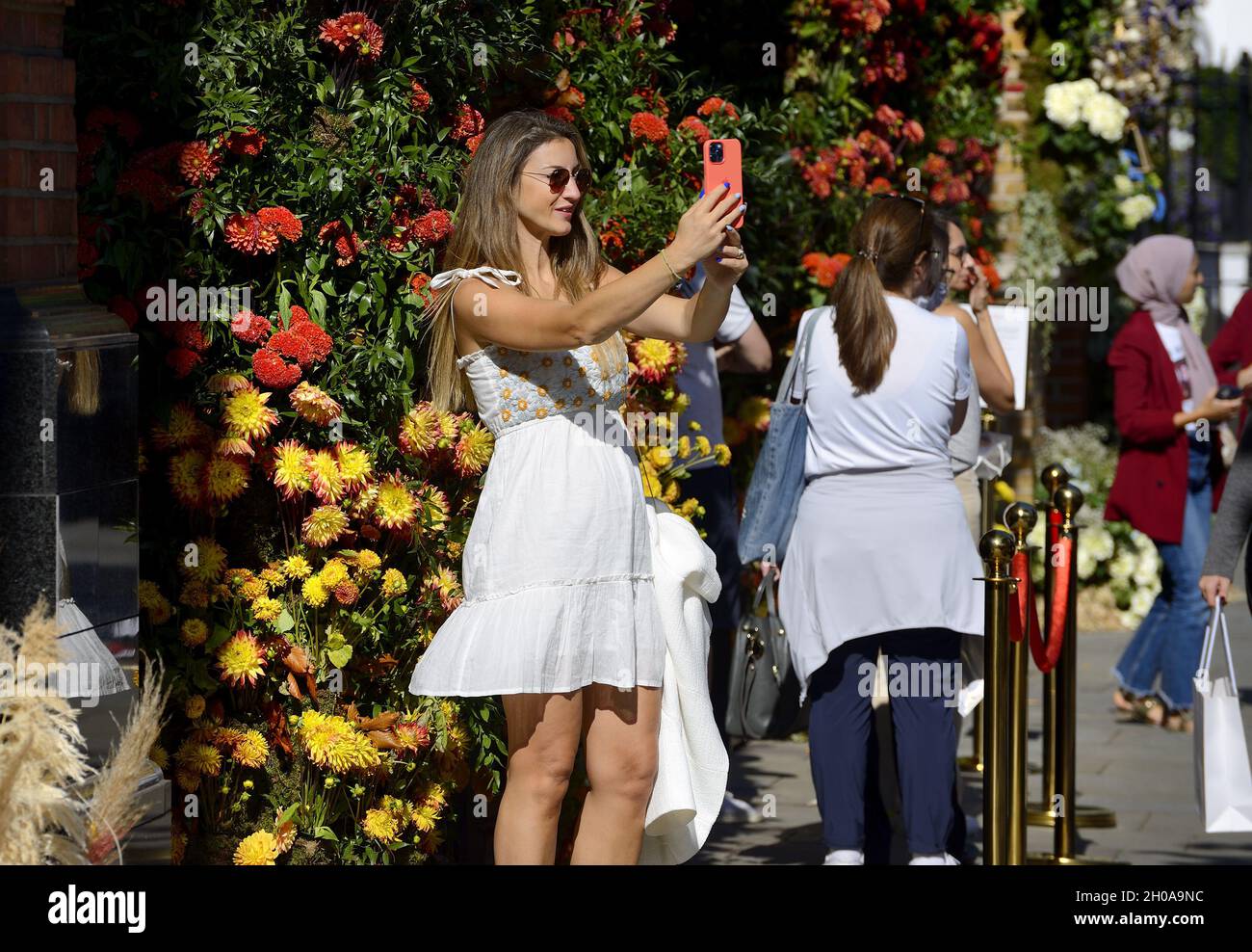 Die junge Frau, die während der jährlichen Blumenkunstshow Chelsea in Bloom ein Selfie auf ihrem Handy machte, und die Blumendusche in den Geschäften und Straßen von Chelsea Stockfoto