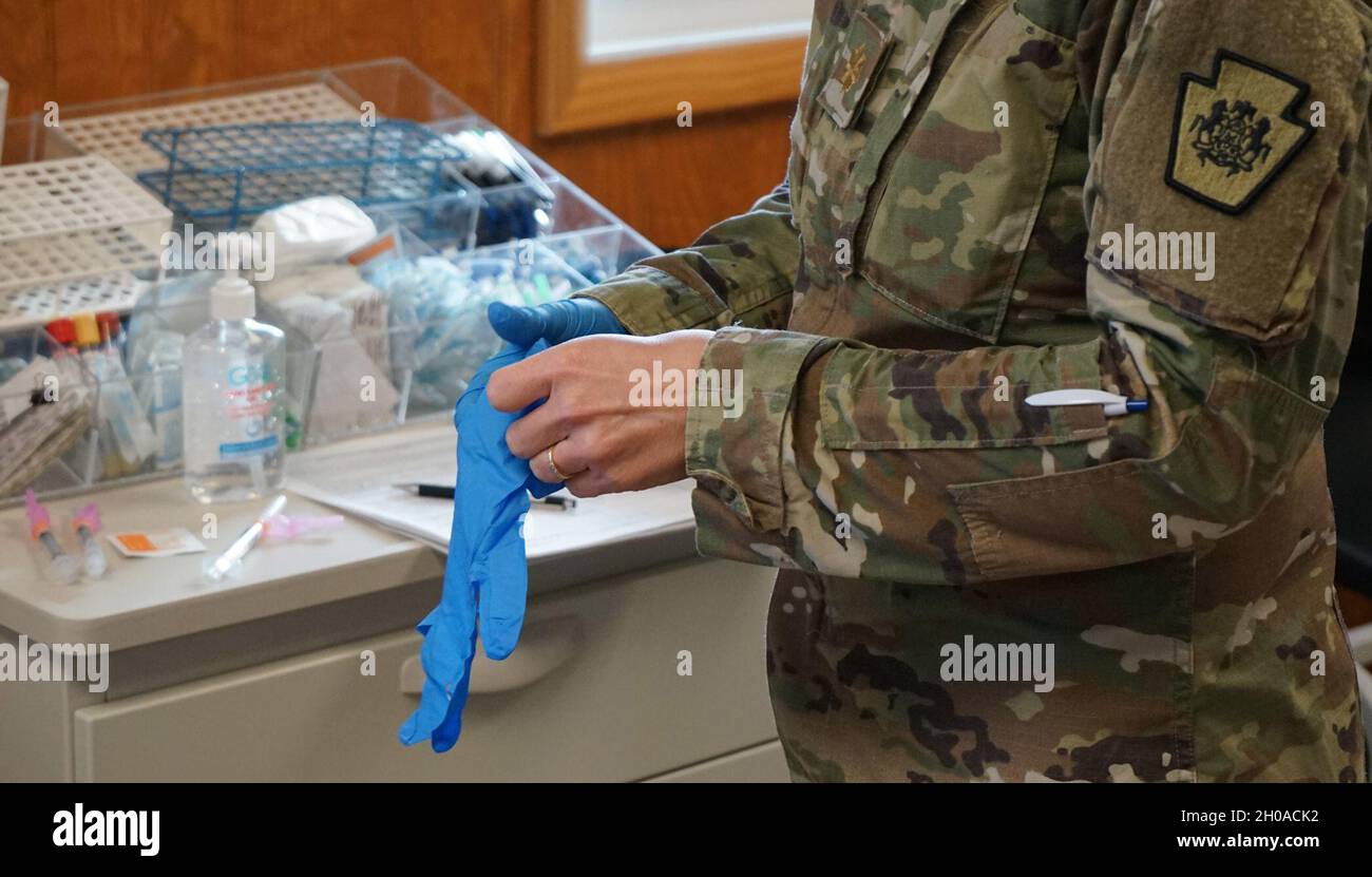Maj. Michelle Nyameke, eine eingetragene Krankenschwester bei der medizinischen Abteilung der Pennsylvania National Guard, zieht ein Paar Handschuhe an, um sich darauf vorzubereiten, dem nächsten Soldaten während der Impfungen am 8. Januar 2021 in Fort Indiantown Gap, Pennsylvania, eine Dosis COVID-19-Impfstoff zu verabreichen. Soldaten und Luftwaffe wurden untersucht und ihre Aufzeichnungen aktualisiert, um alle am Impfprozess beteiligten Dienstmitglieder zu schützen. Stockfoto