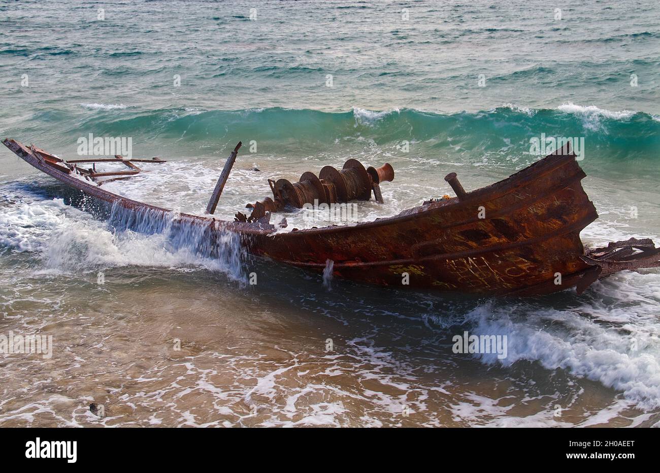 Wellen, die auf das rostige Wrack eines gebrochenen, gestrandeten Fischerbootes spritzen Stockfoto
