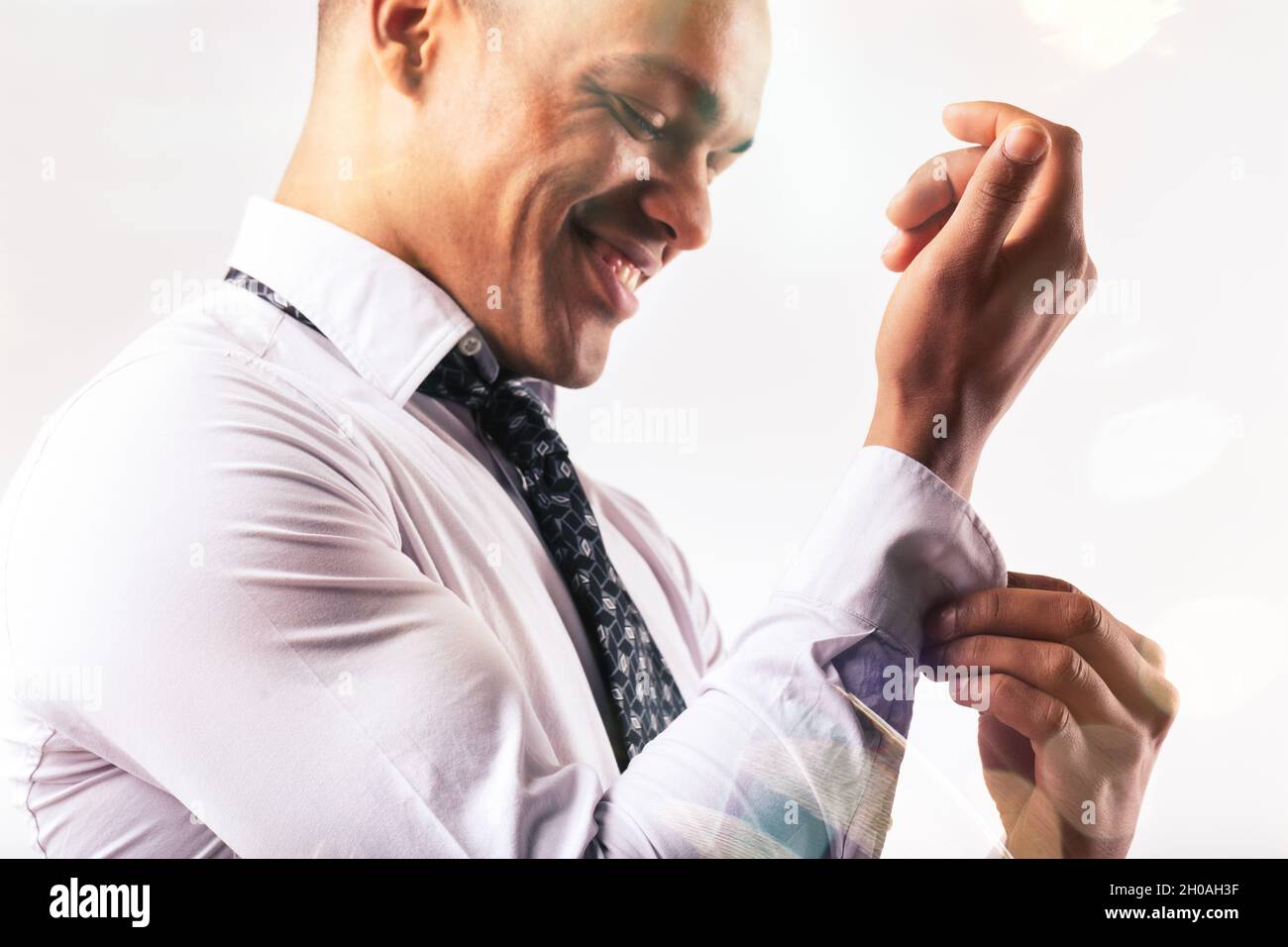 Kurze Nahaufnahme eines glücklichen jungen schwarzen Mannes, der sich in einem High-Key-Portrait mit dem Knopf auf dem Ärmel seines Hemdes verkleidet Stockfoto