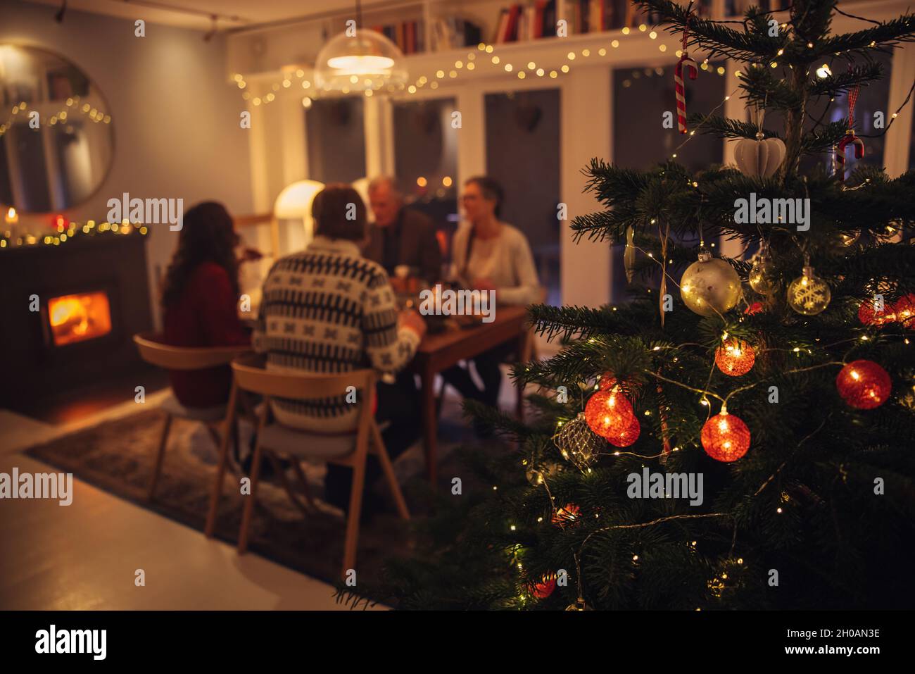 Innenansicht eines warmen und gemütlichen skandinavischen Hauses, das für Weihnachtsfeiern dekoriert ist. Konzentrieren Sie sich auf geschmückten Weihnachtsbaum mit Familie beim Abendessen Stockfoto