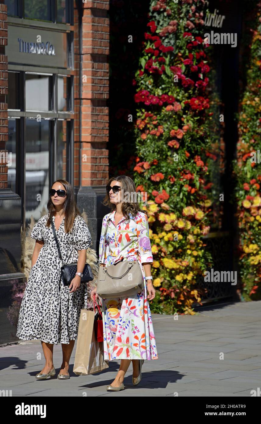 Frauen, die an Tiffany und Co auf dem Sloane Square vorbeilaufen, während der jährlichen Blumenkunstshow Chelsea in Bloom und der Blumendusche in den Geschäften und Straßen von Chelse Stockfoto