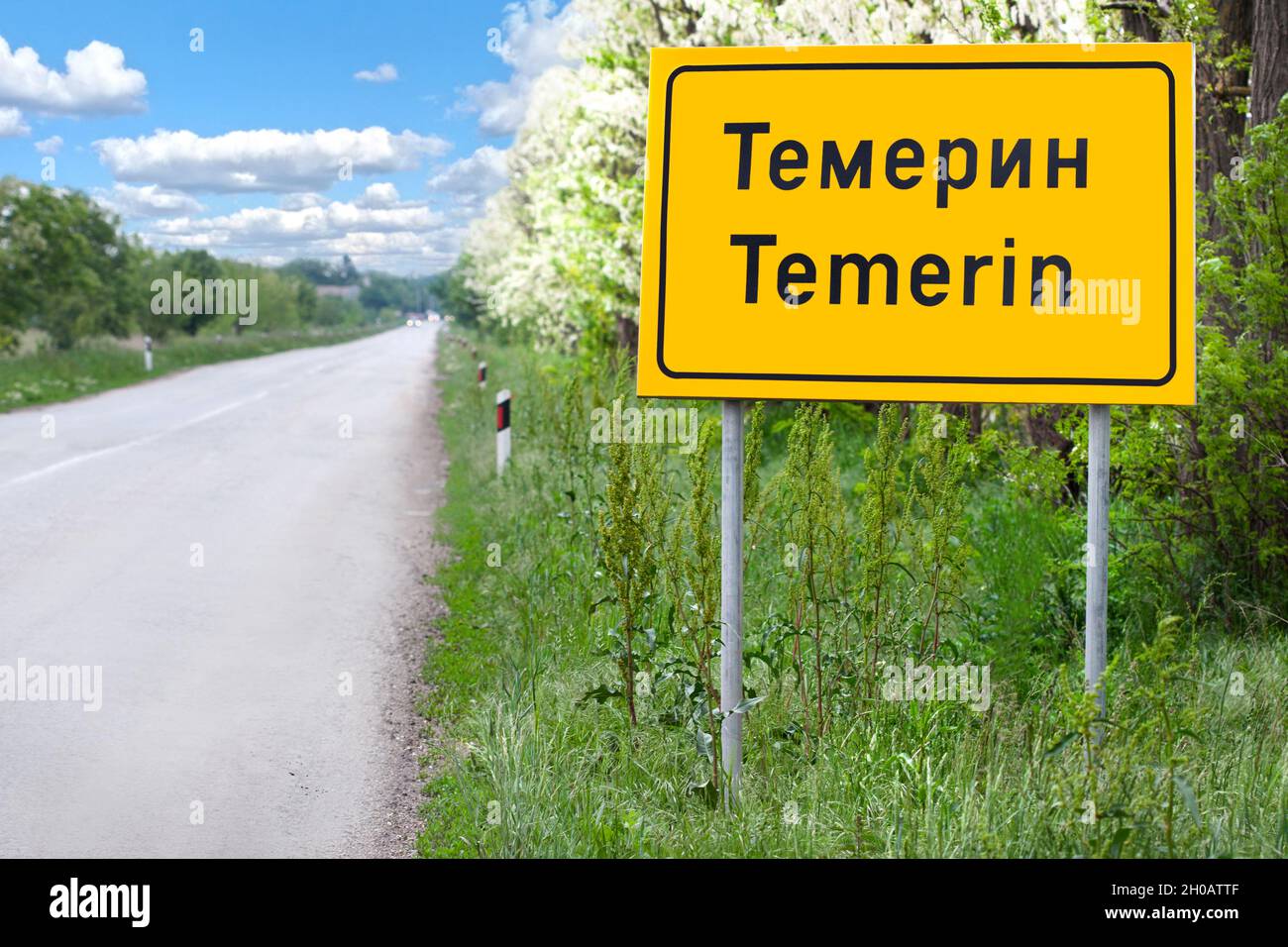 Temerin Stadtschild entlang der Straße an einem schönen Frühlingstag. Temerin Ortsname in kyrillischen und lateinischen Buchstaben, Vojvodina, Serbien.Gelber Brett Stadtname Stockfoto