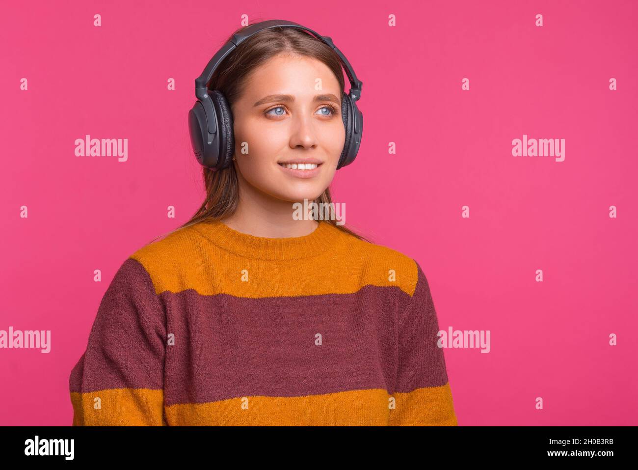 Die junge Frau trägt einen Kopfhörer und hört Musik, Hörbücher oder Podcasts auf rosa Hintergrund. Stockfoto