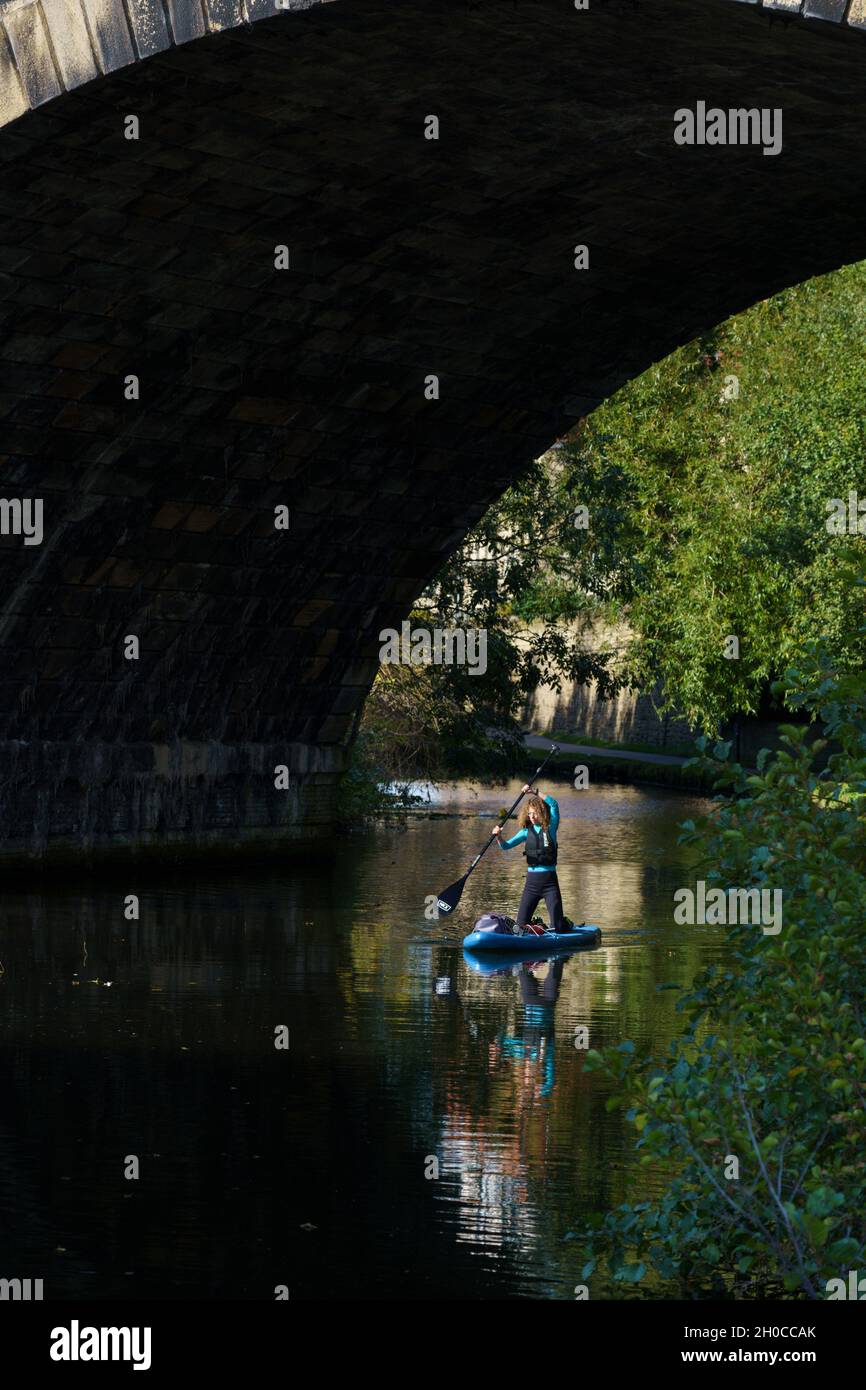 Unter einem stillgelegten Eisenbahnviadukt am Leeds und Liverpool Canal rudert eine energiegeladene Frau in Leeds, West Yorkshire, Großbritannien, ein Paddleboard. Stockfoto