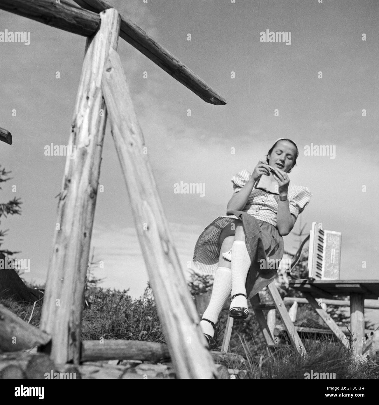 Eine junge Frau sitzt mit einem Akkordeon ein einem Zaun, Deutschland 1930er Jahre. Eine junge Frau durch einen Zaun mit einem Akkordeon sitzen, Deutschland 1930. Stockfoto