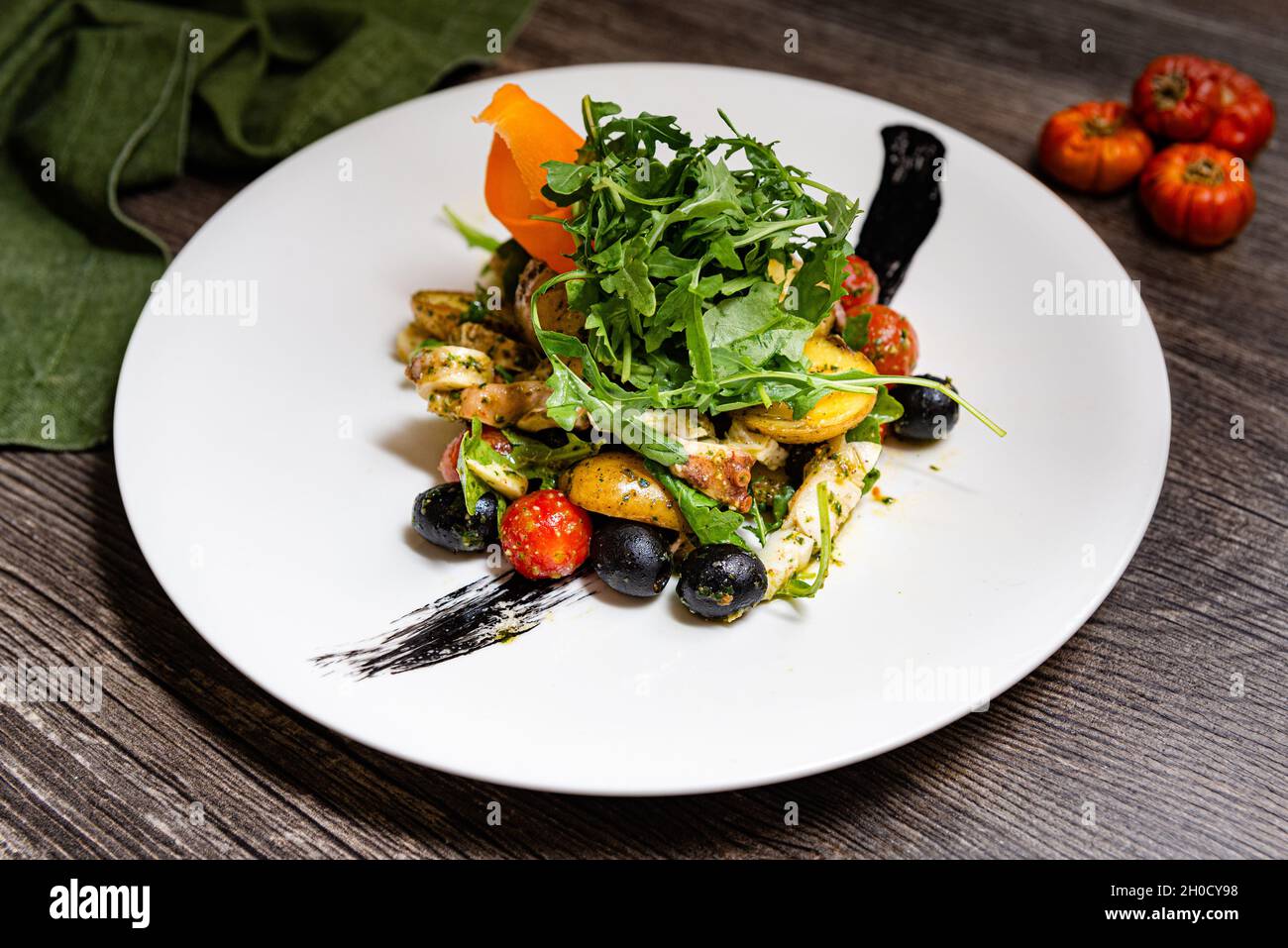Italienischer Salat mit Tintenfisch im ligurischen Stil. Rucola, schwarze Oliven, Kirschtomaten, Tintenfisch-Tentakeln, Babykartoffelscheiben, Tintenfischtinte. Auf einer da Stockfoto