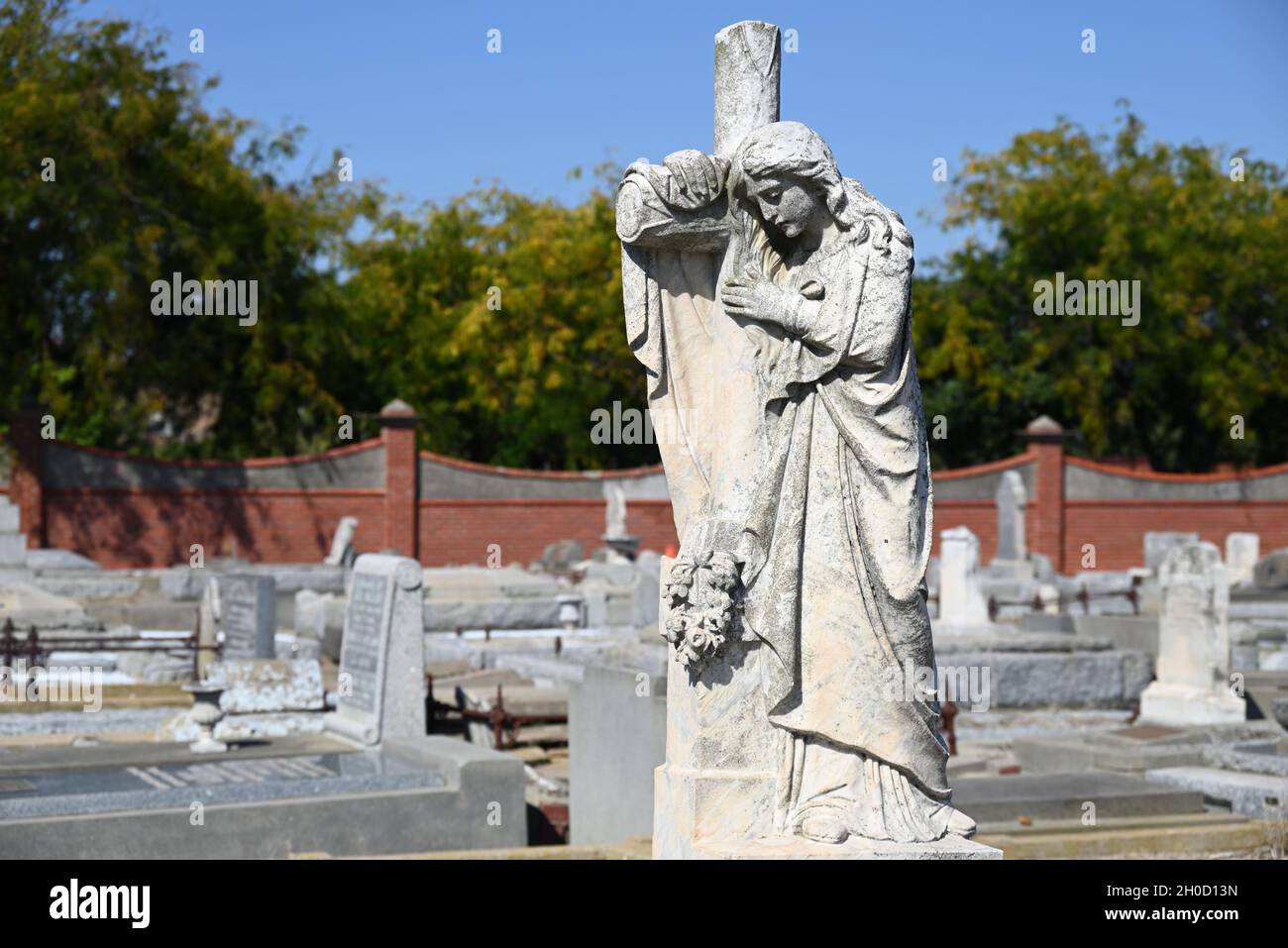Skulptur einer Frau, die an einem sonnigen Tag auf einem Friedhof am Kreuz trauert Stockfoto