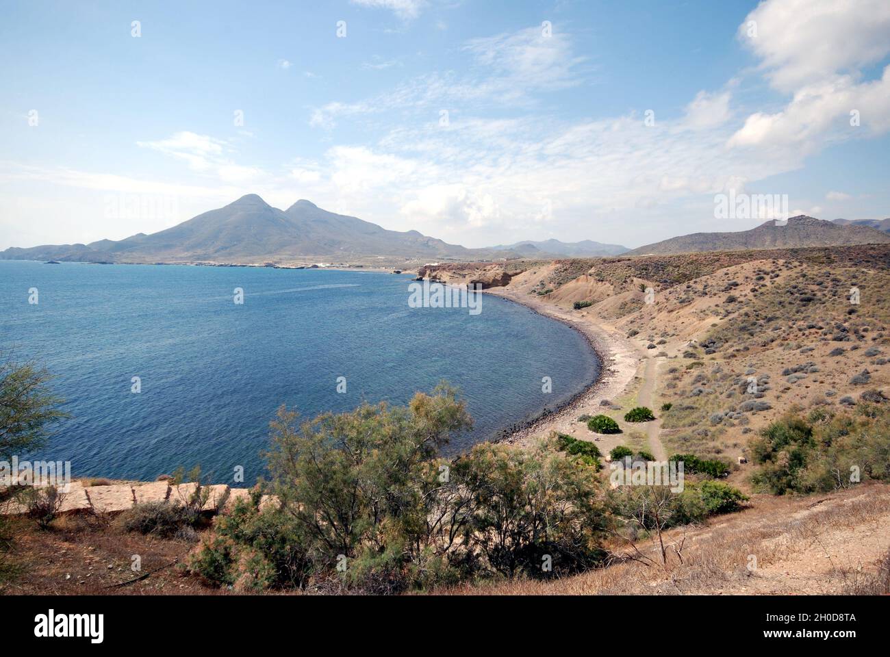 Eine Landschaft mit Blick aufs Meer in Isleta del Moro in Almeria, Andalusien, Spanien mit vulkanischen Hügeln im Hintergrund, typisch für die Landschaft von Cabo de Gata. Stockfoto