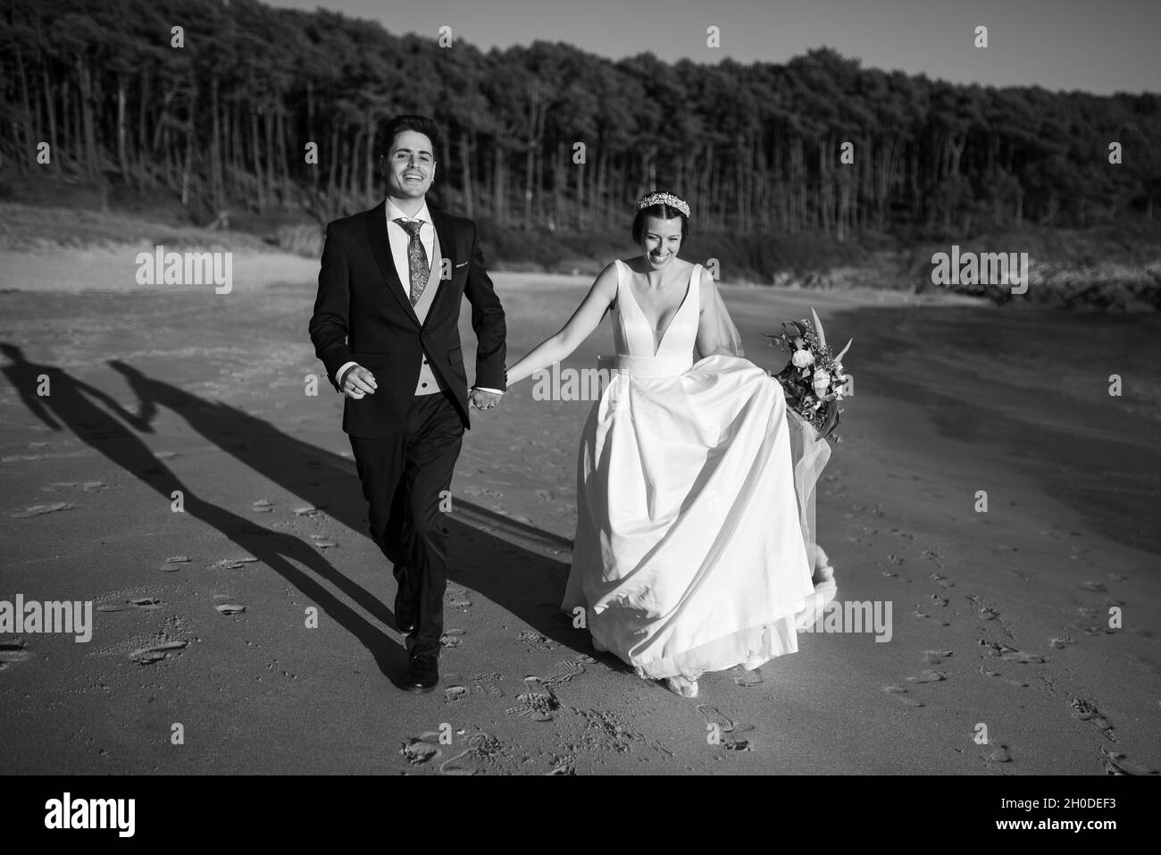 Gerade verheiratetes Paar, das an einem Strand auf schwarz und weiß läuft Stockfoto