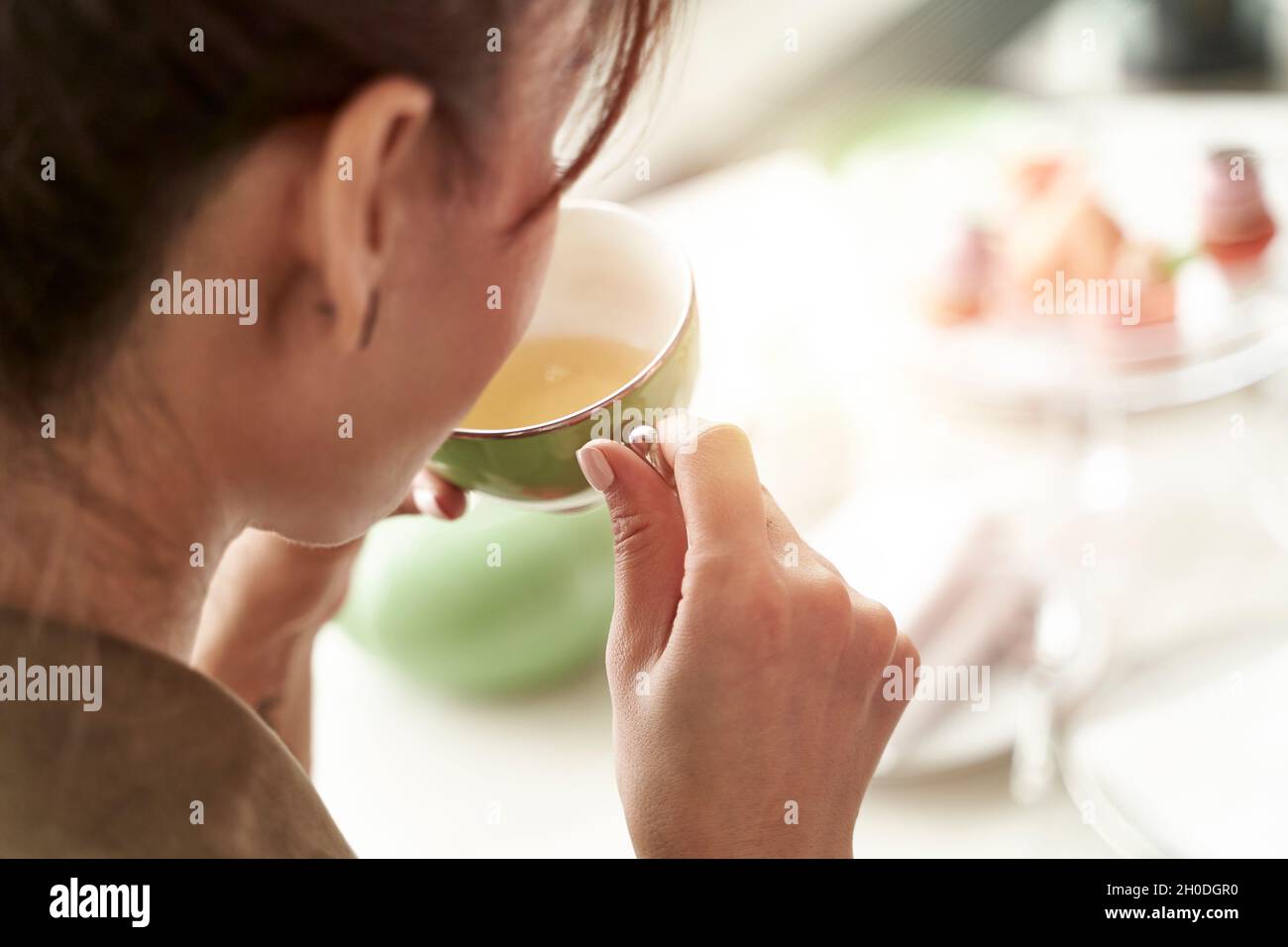 Nahaufnahme der Rückseite einer asiatischen Frau, die am Tisch sitzt und Tee aus einer grünen Teetaße trinkt Stockfoto