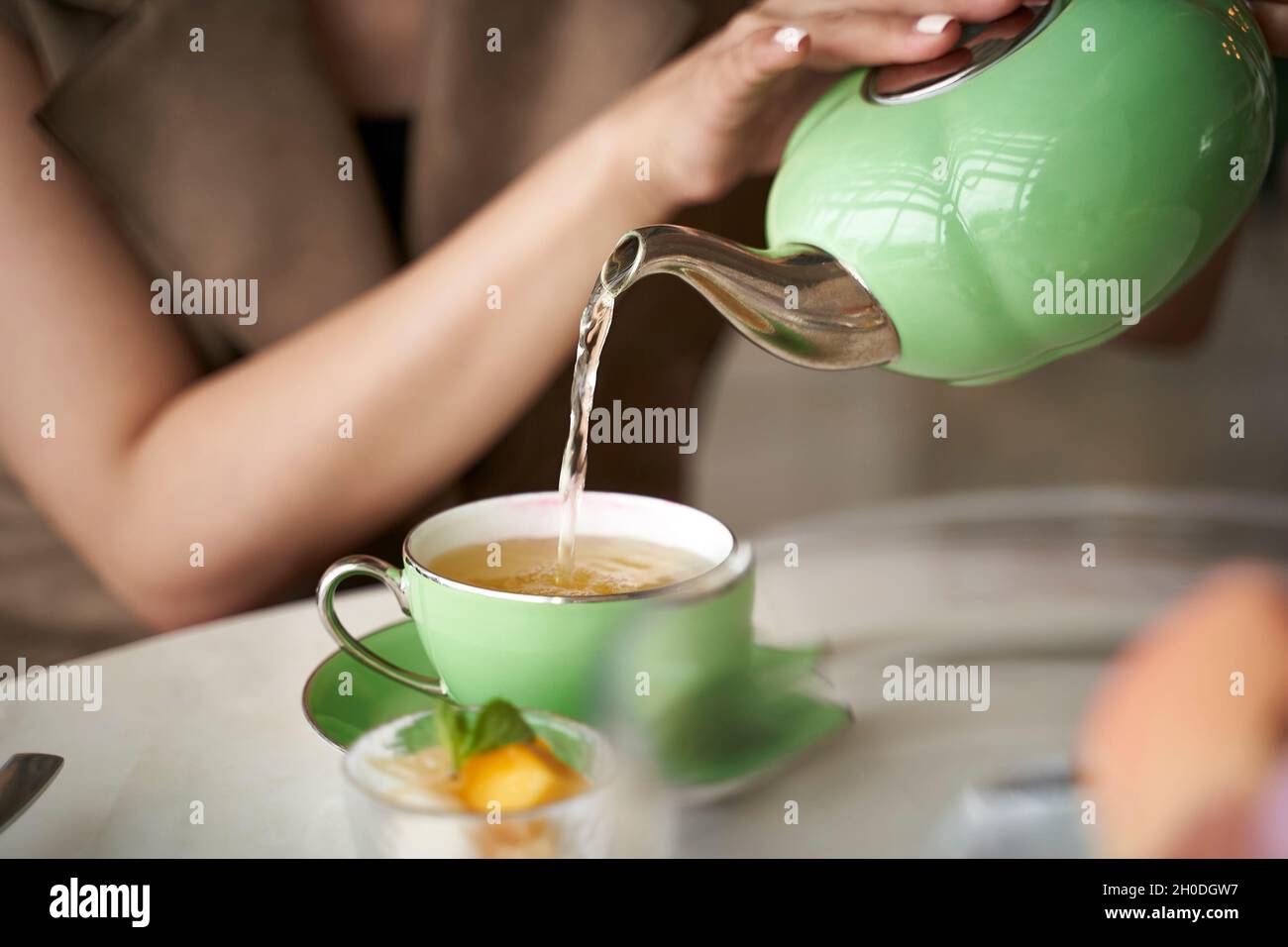 asiatische Frau, die am Tisch sitzt und eine Teetaße mit Tee füllt Stockfoto