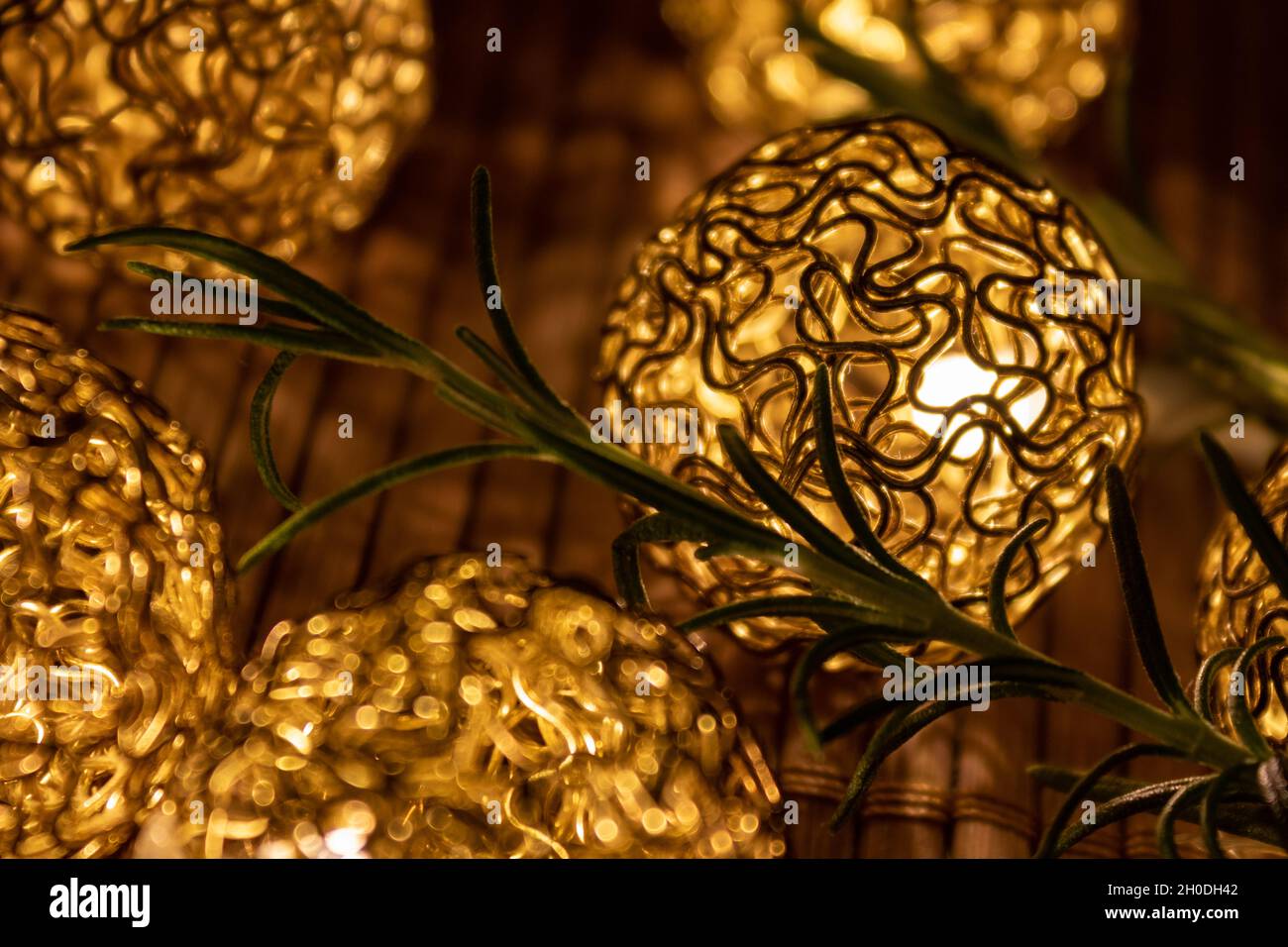 Beleuchtete goldene weihnachtskugeln mit Tannenzweig auf Holztisch, Nahaufnahme. Festlich eleganter Hintergrund Stockfoto