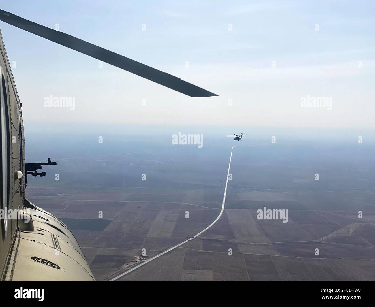 Ein Hubschrauber der Serie UH-60 Black Hawk, der von Soldaten mit dem Assault Helicopter Bataillon der 28. Expeditionary Combat Aviation Brigade betrieben wird, ist durch das Fenster eines Hubschraubers der Serie CH-47 Chinook sichtbar, während sie über das Einsatzgebiet des 28. ECAB im Nahen Osten fliegen. Stockfoto