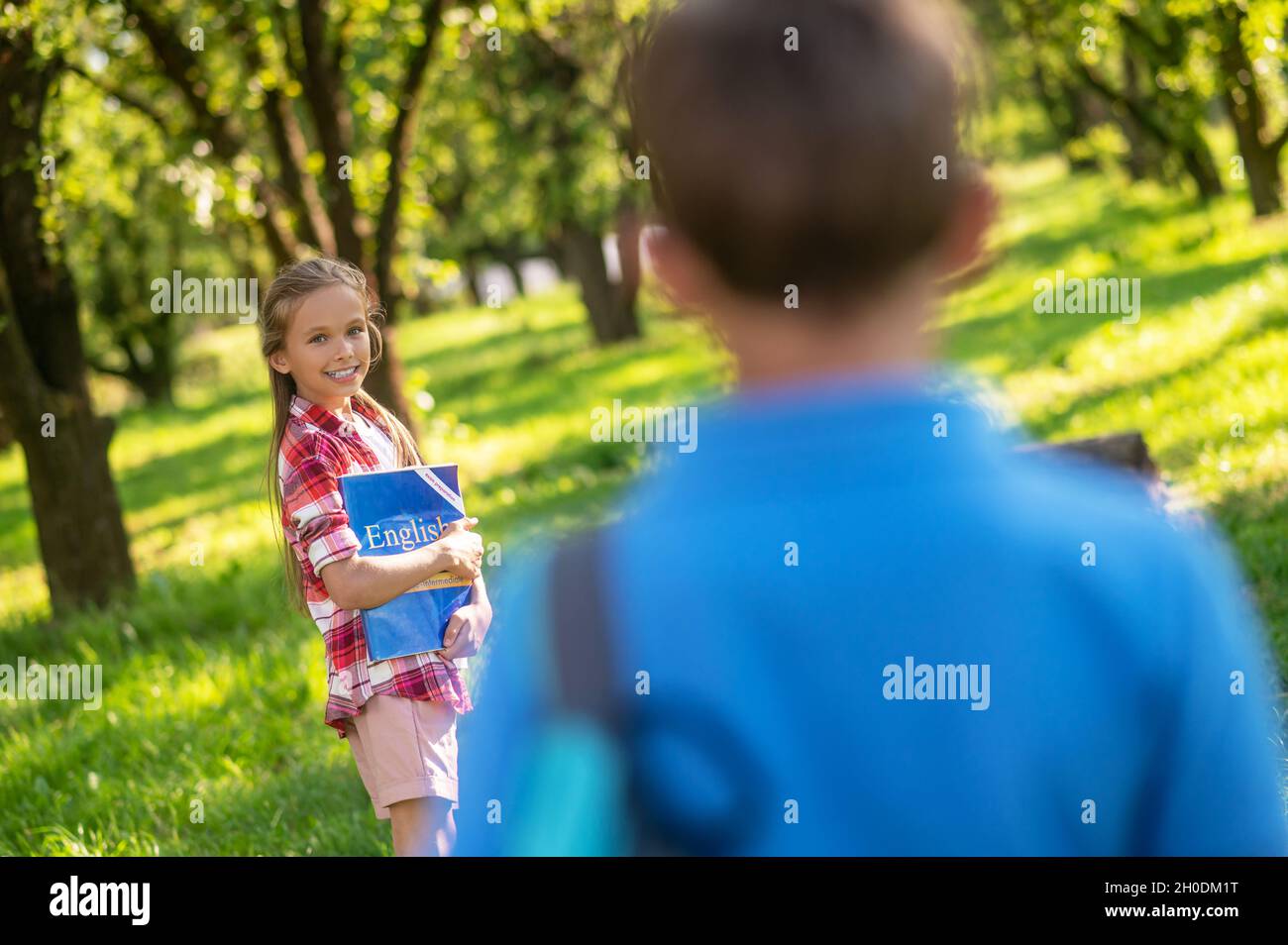 Nettes Mädchen mit Lehrbuch und Junge zurück zur Kamera Stockfoto