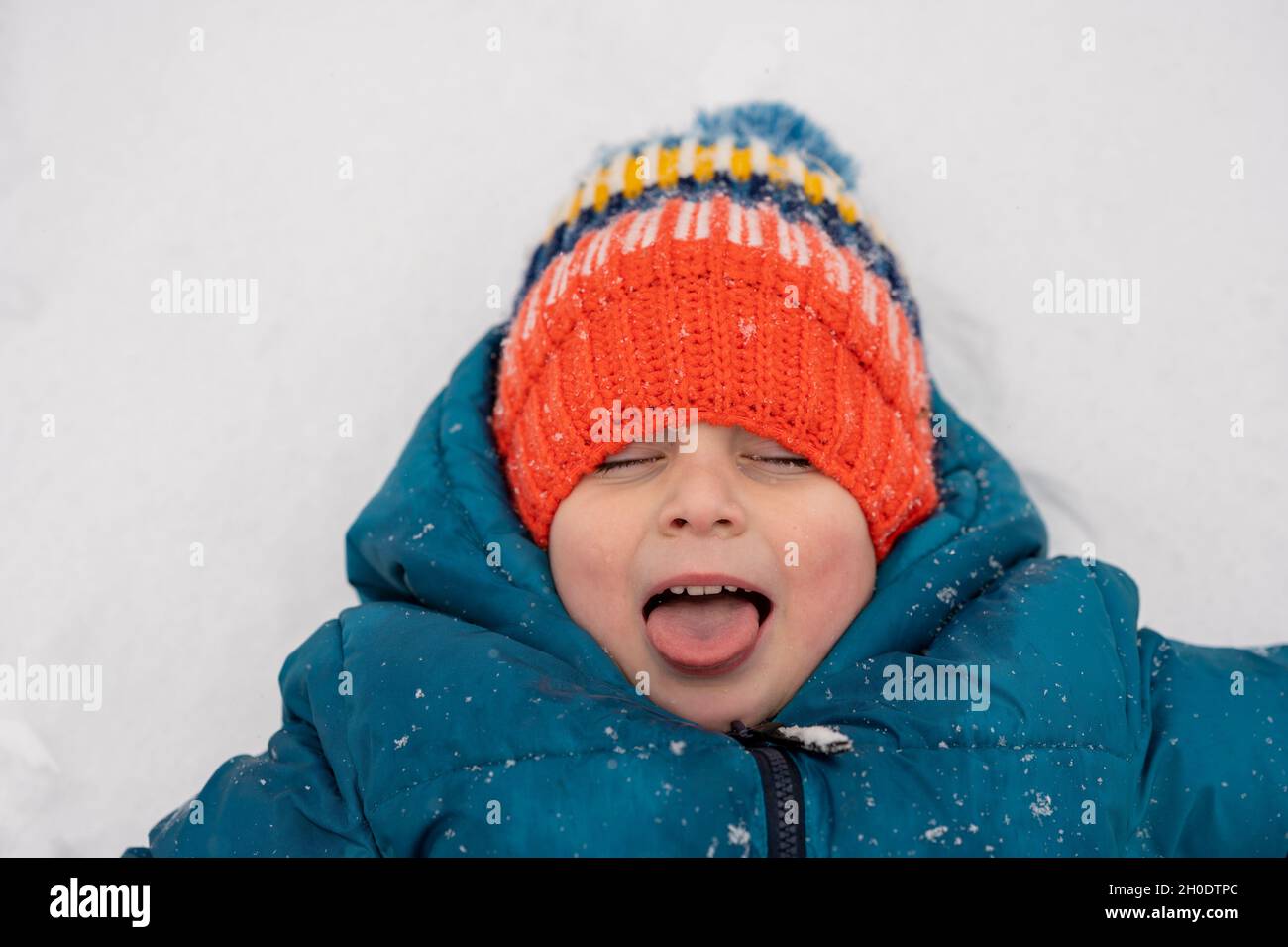 Kleiner Junge in Strickmütze fängt Schneeflocken auf seiner Zunge Stockfoto