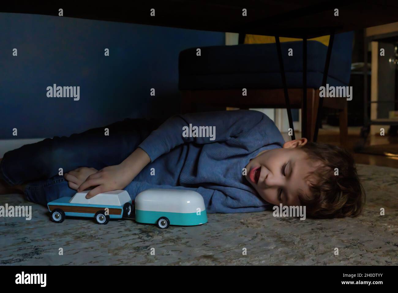 Junge spielt mit dem Spielzeugauto unter dem Couchtisch auf dem Teppich im Wohnzimmer Stockfoto